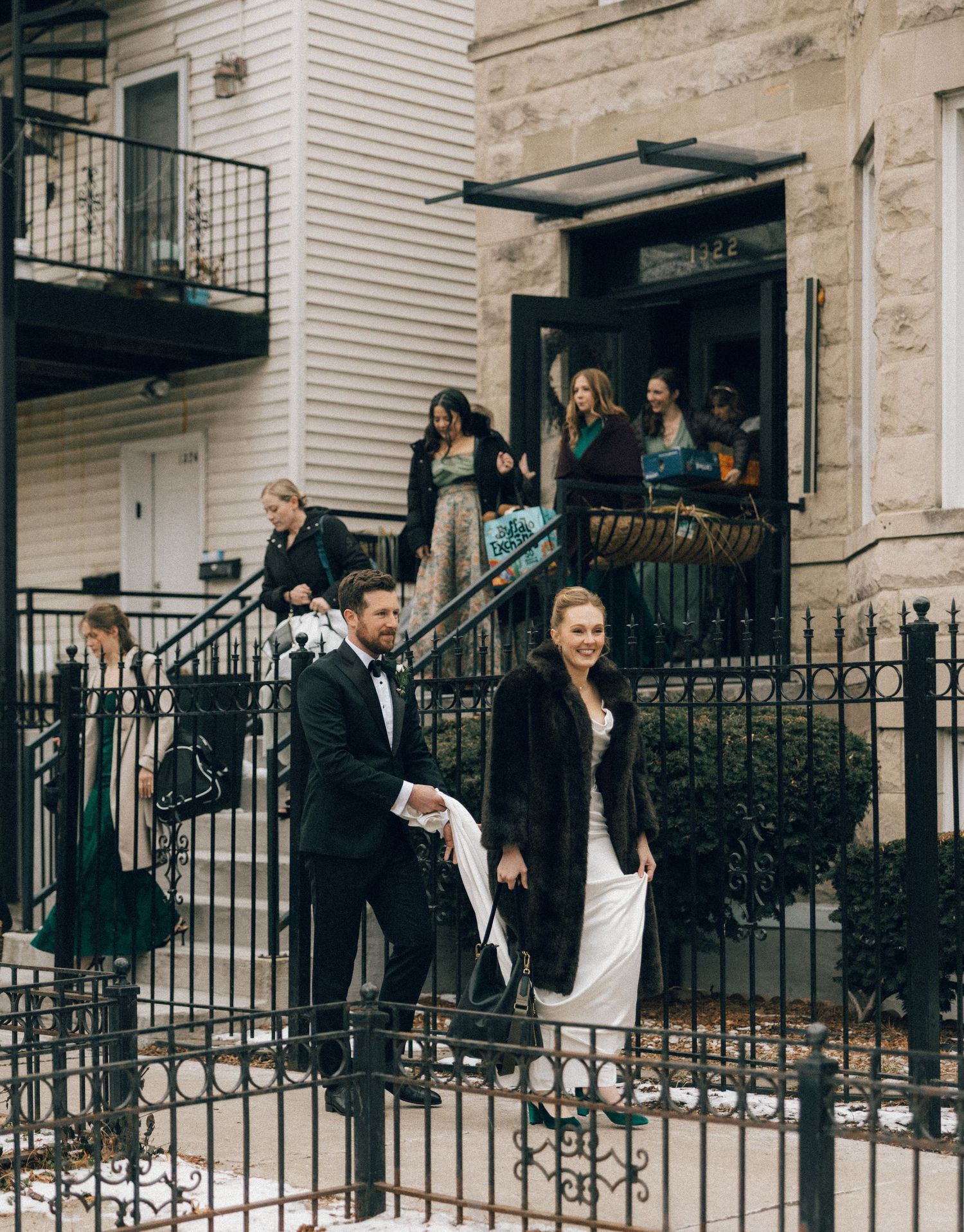 Wedding party members in formal attire walking down outdoor steps of a residential building.