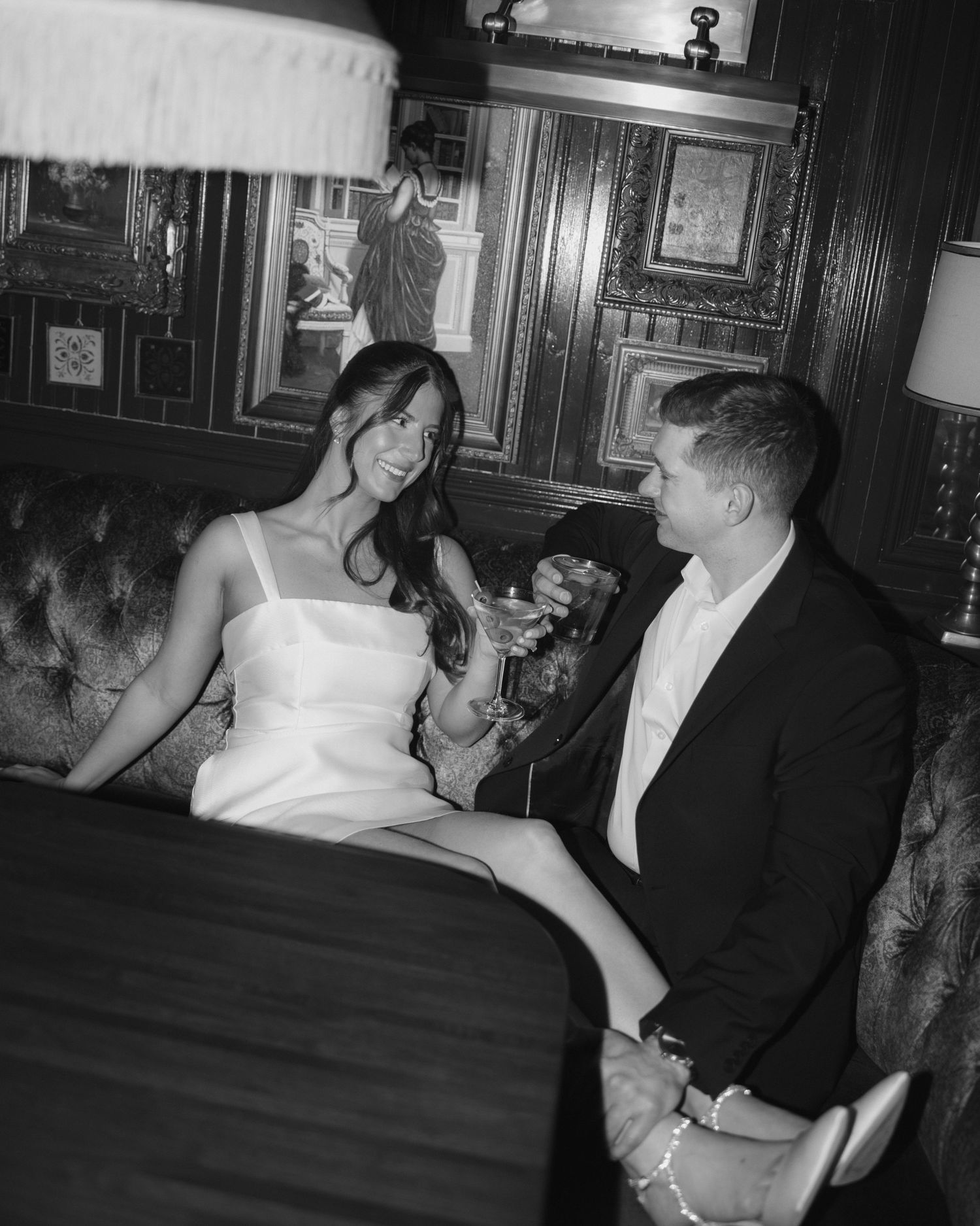 A couple in formal attire share an intimate moment on an elegant couch in a vintage black and white photograph.