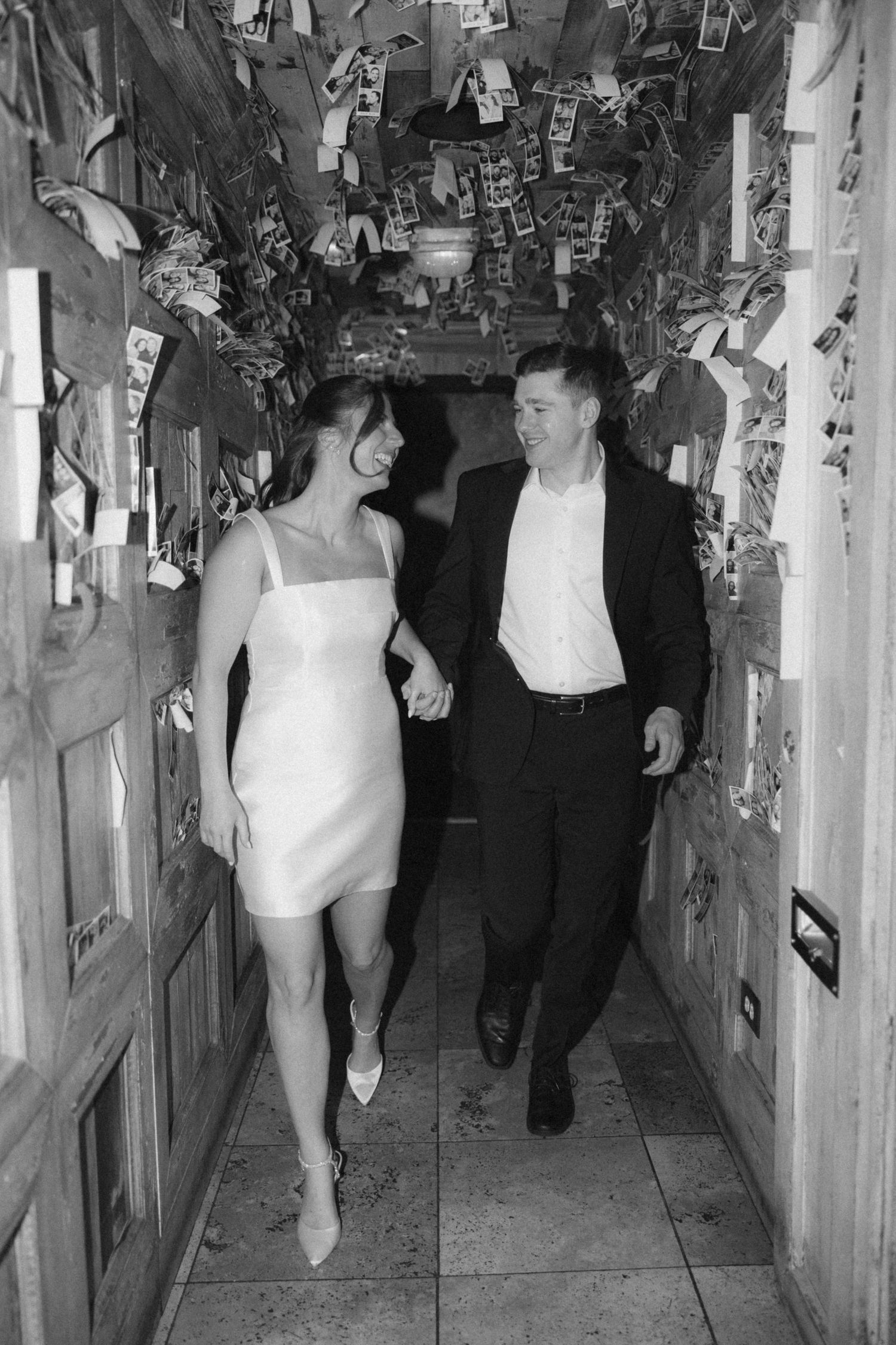 A couple walks together through a narrow hallway decorated with photos and memorabilia on the walls.