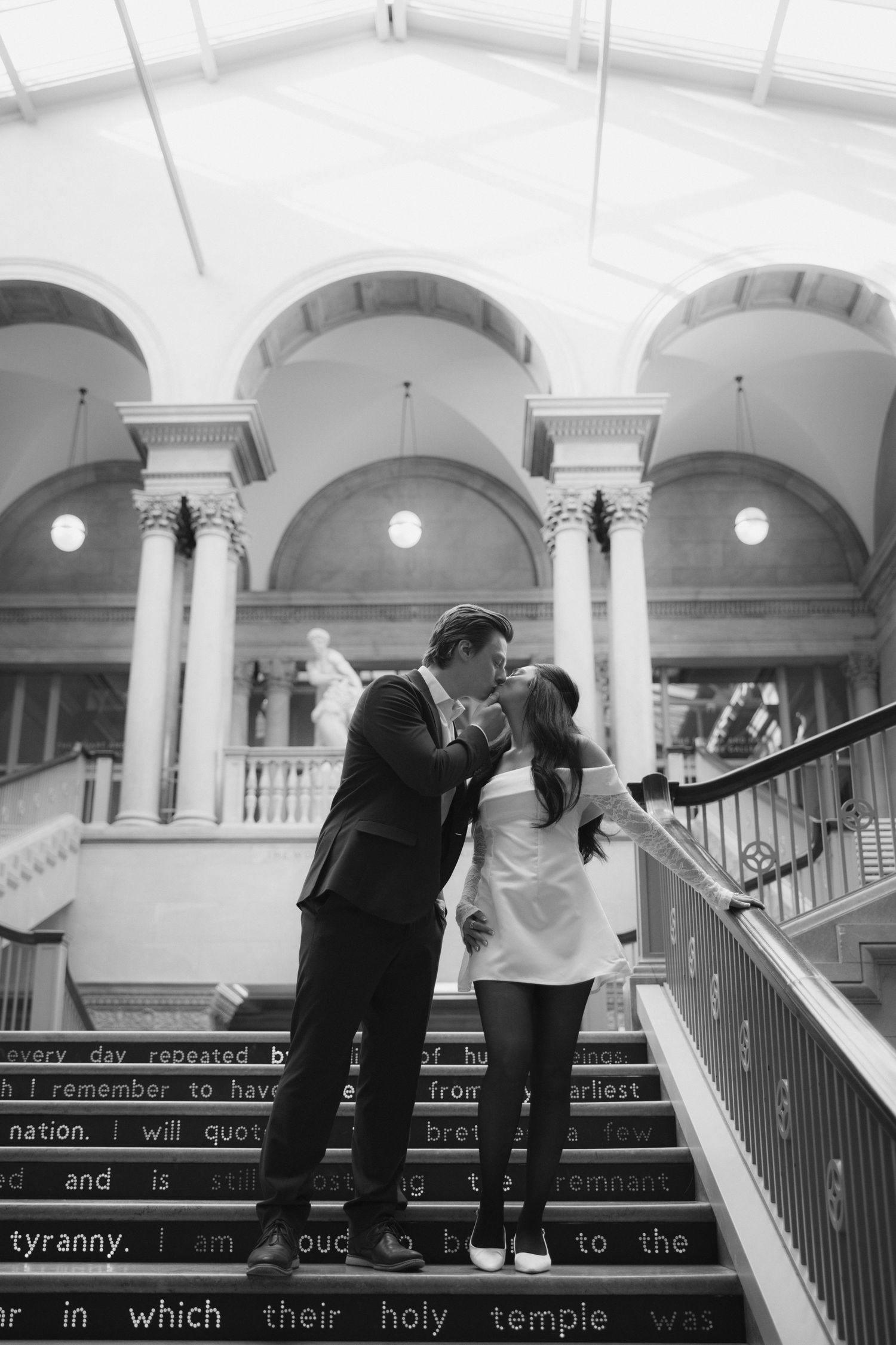 A romantic black and white photo of a couple on a grand staircase with classical architecture.
