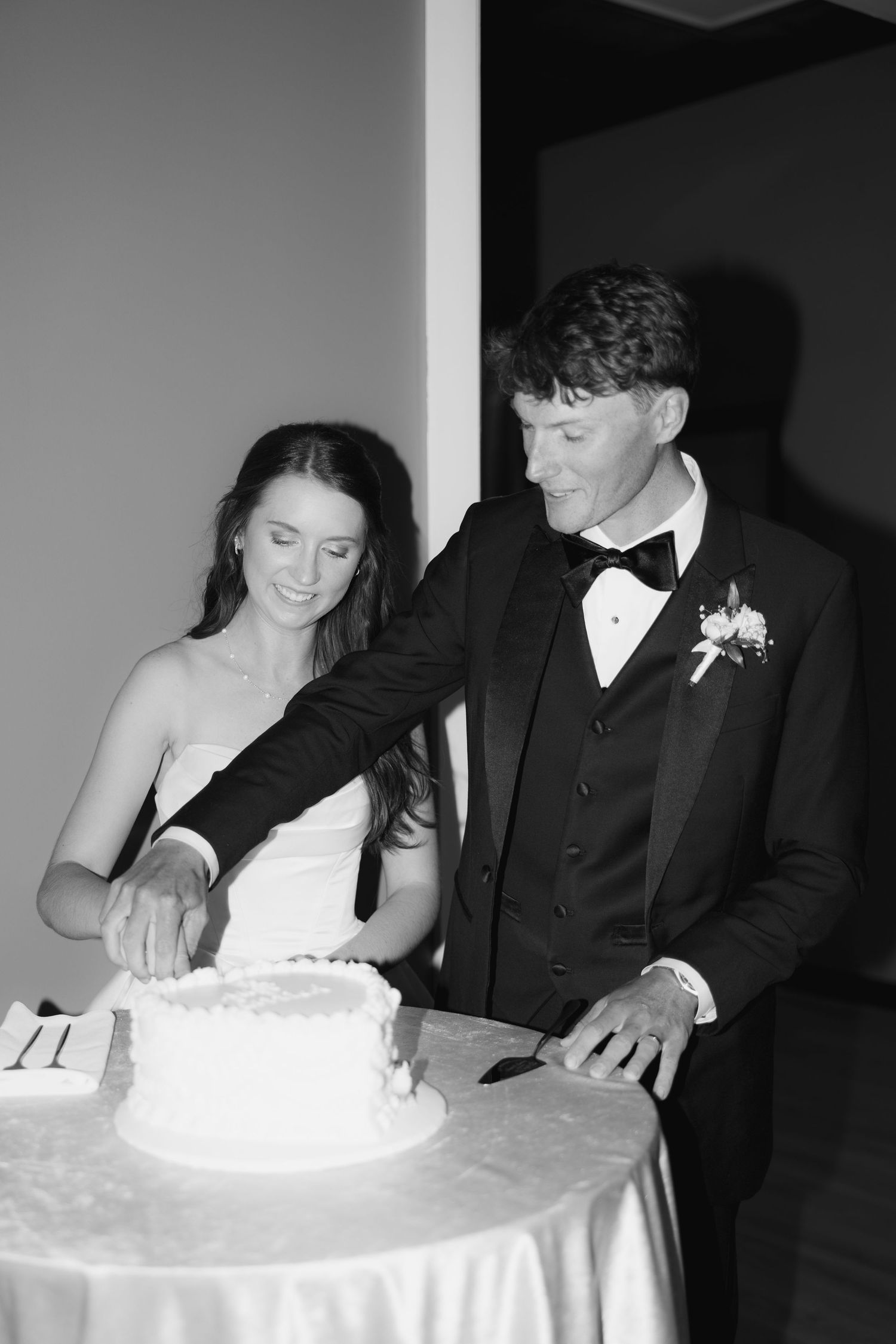 Black and white photo of a bride and groom cutting their wedding cake together at their reception.