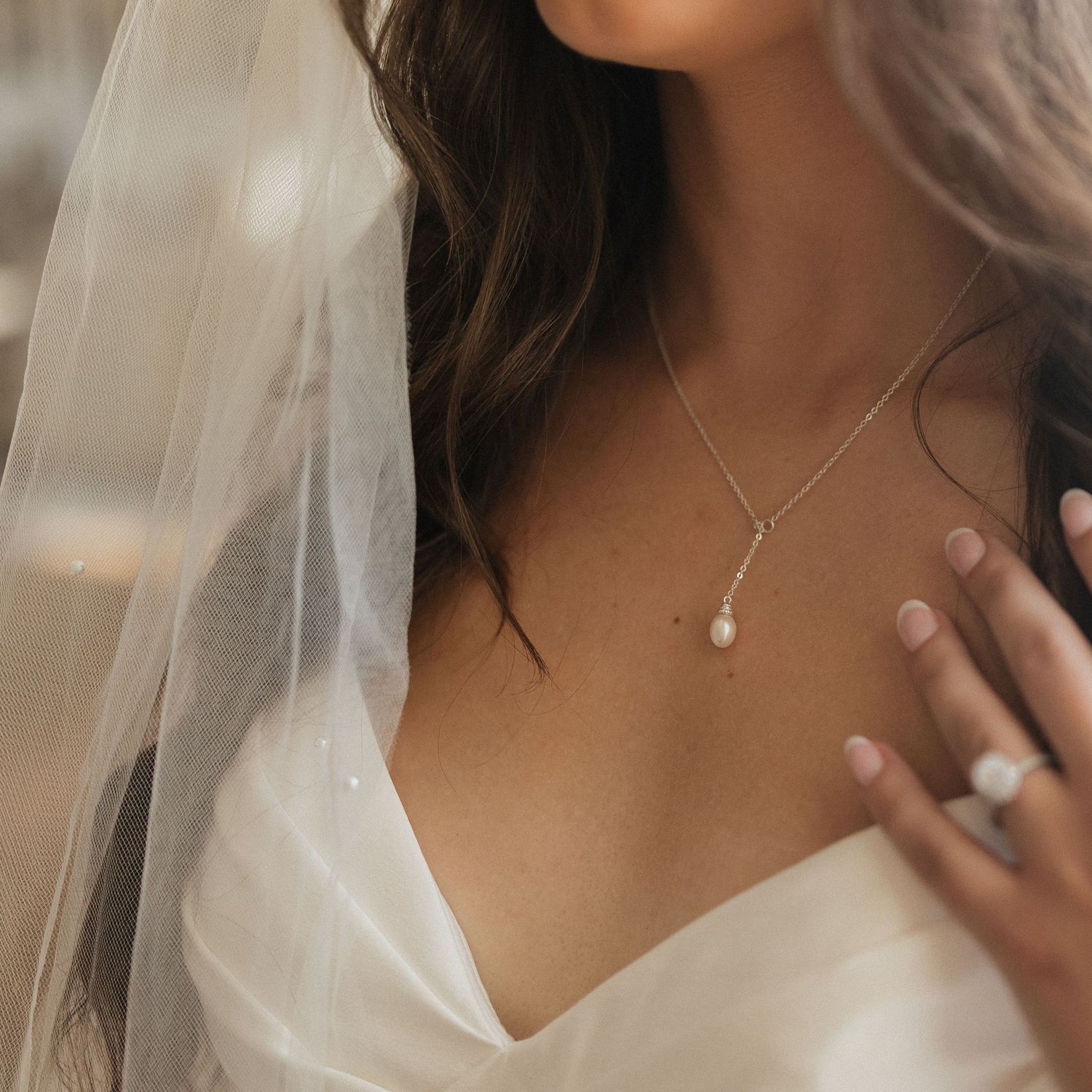 Close-up of a bride wearing a delicate pearl drop necklace with sheer veil and white wedding dress.