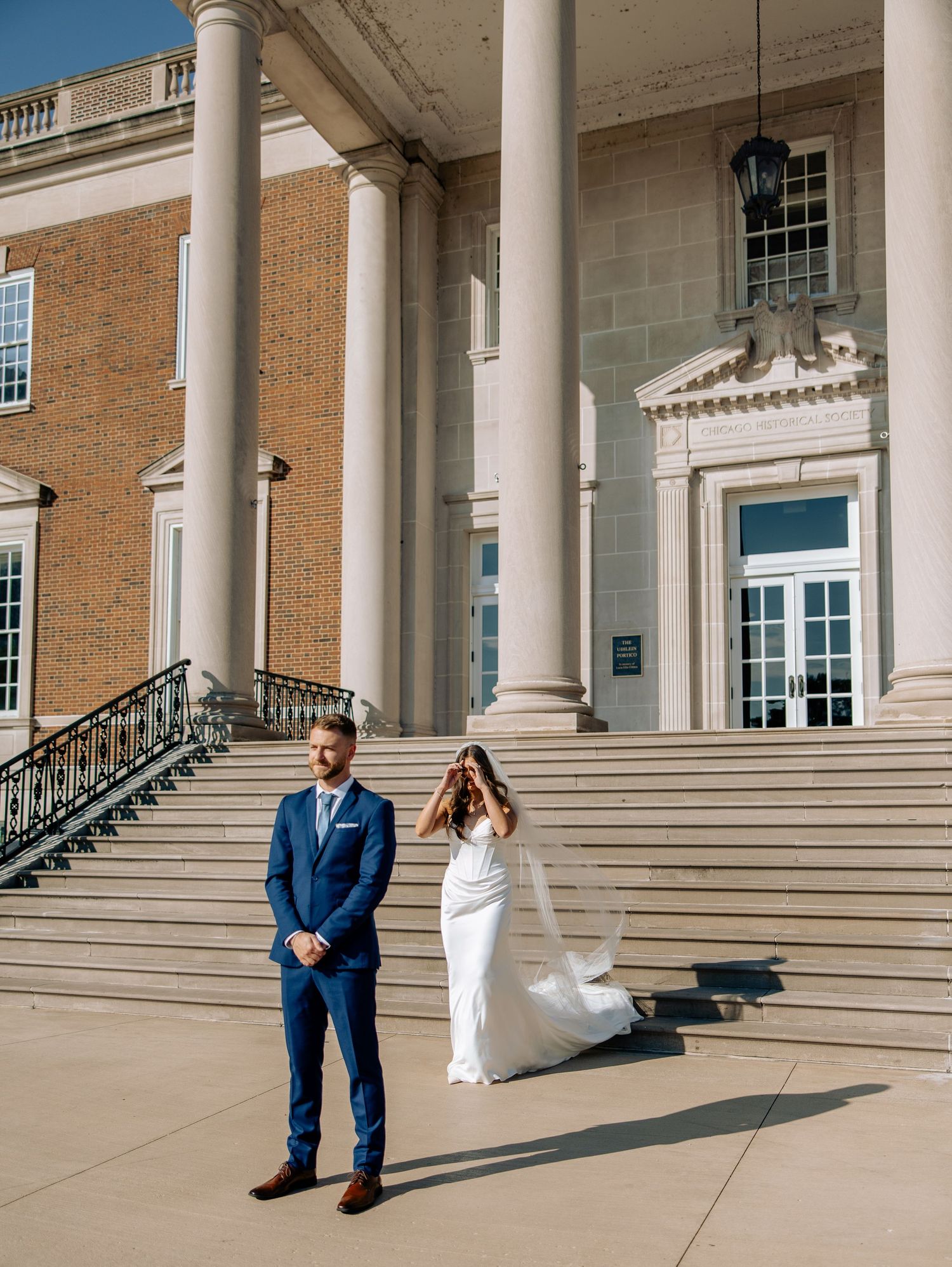 Elegant wedding couple shares romantic moments on grand stone steps of historic brick building with white columns.