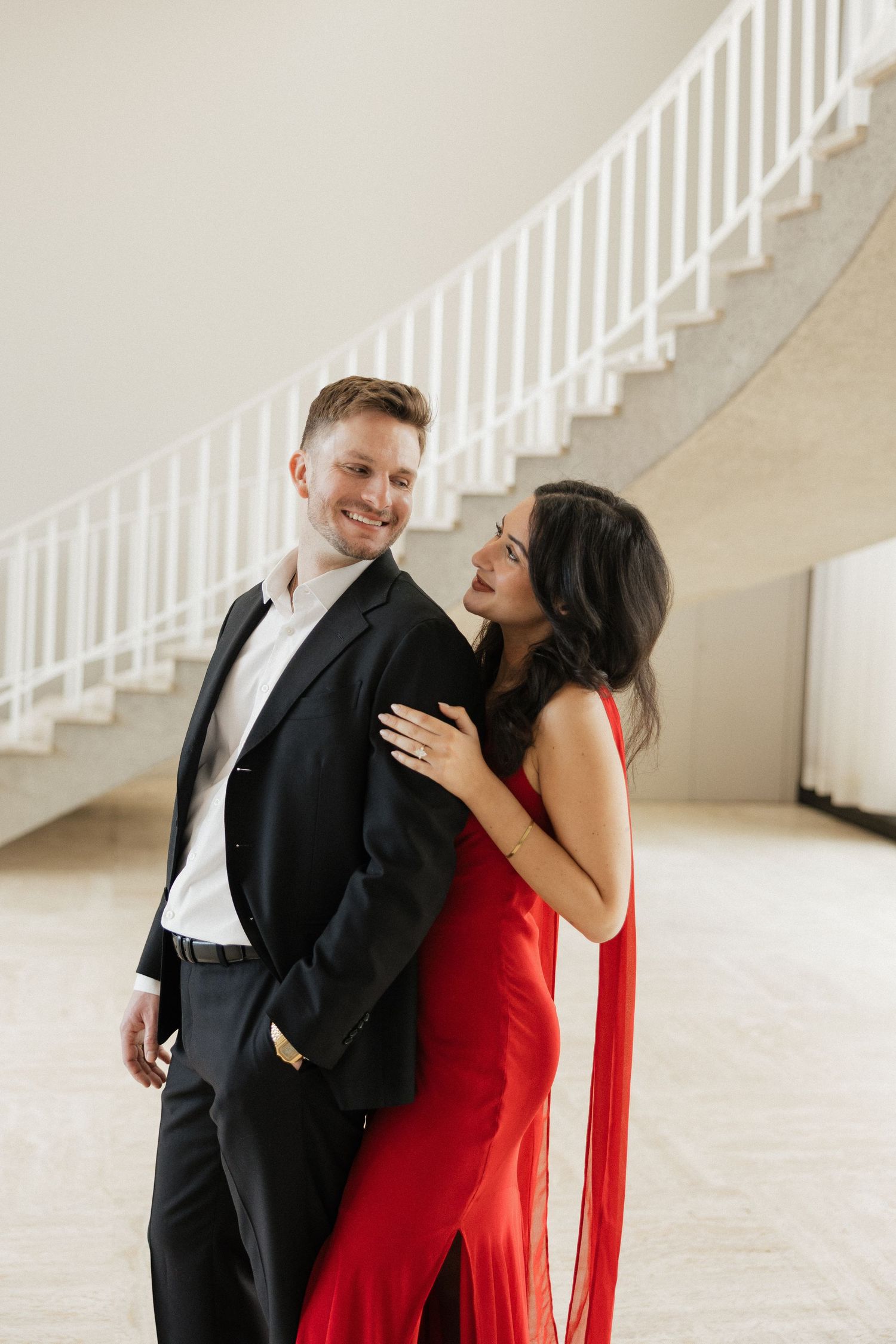 A romantic sequence of photos featuring a couple in black suit and red dress posing against white stairs.