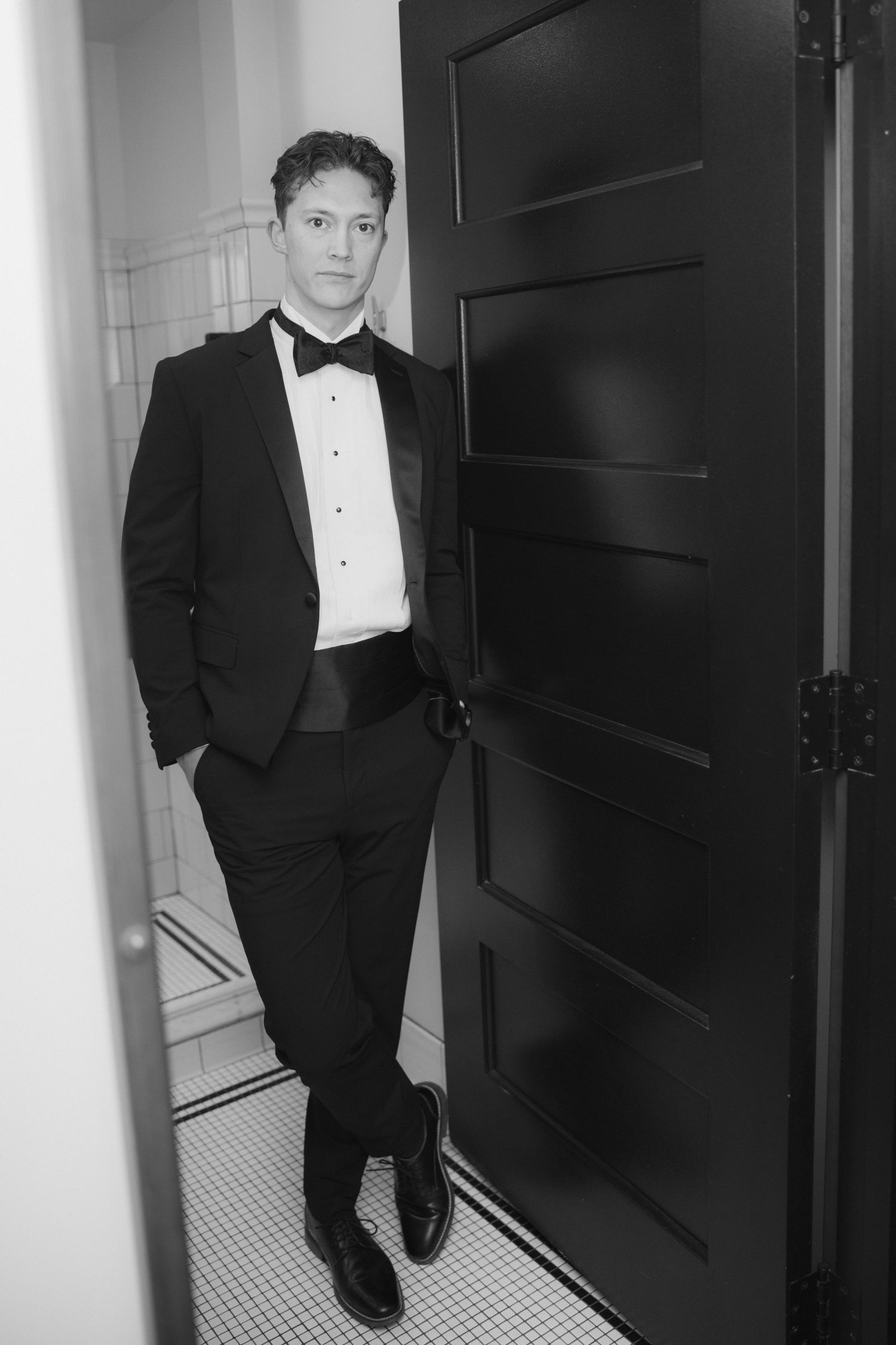 Black and white photos of a person in formal tuxedo standing in a hallway.