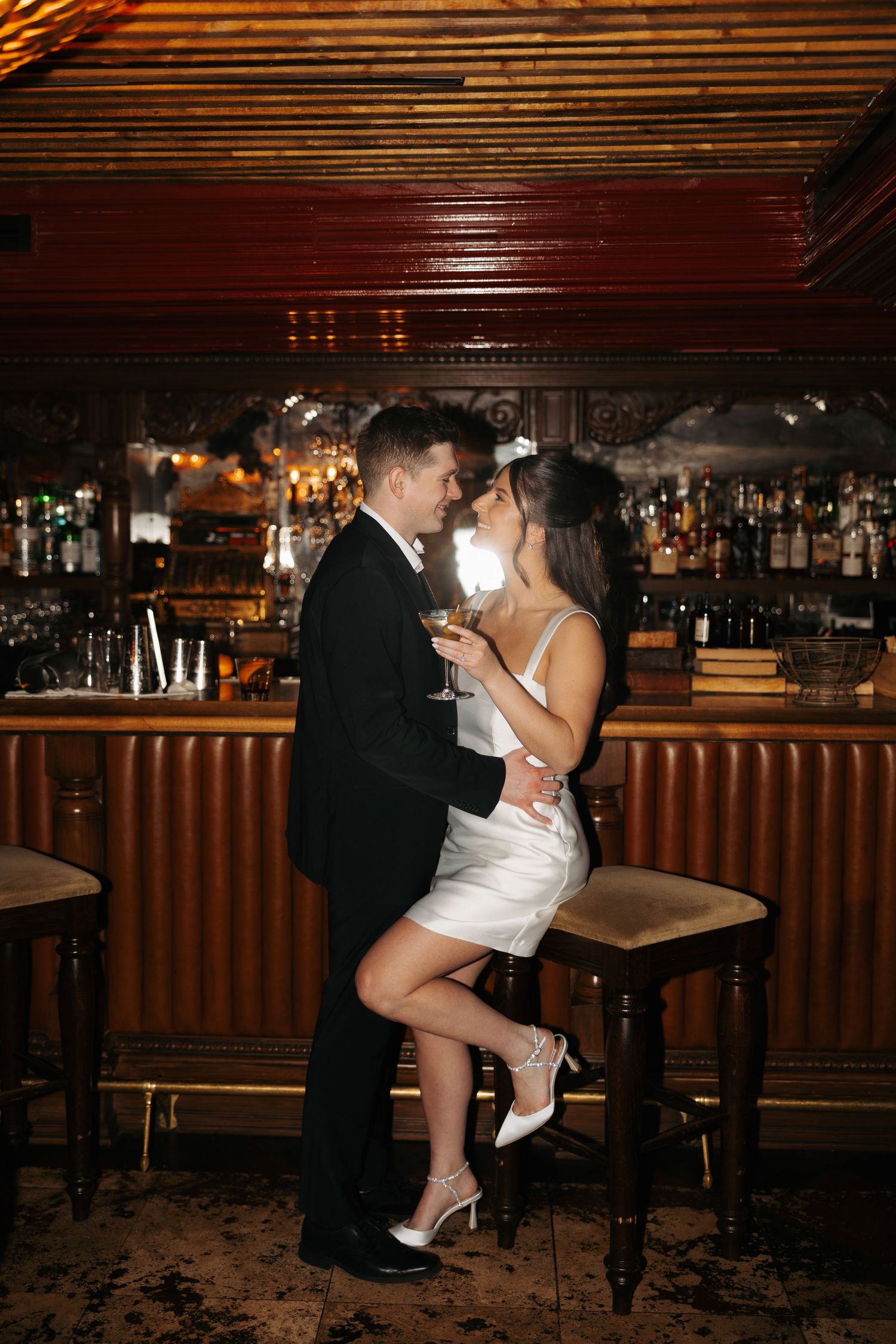 Couple shares an intimate dance moment at a dimly lit bar with wooden decor and barstools.