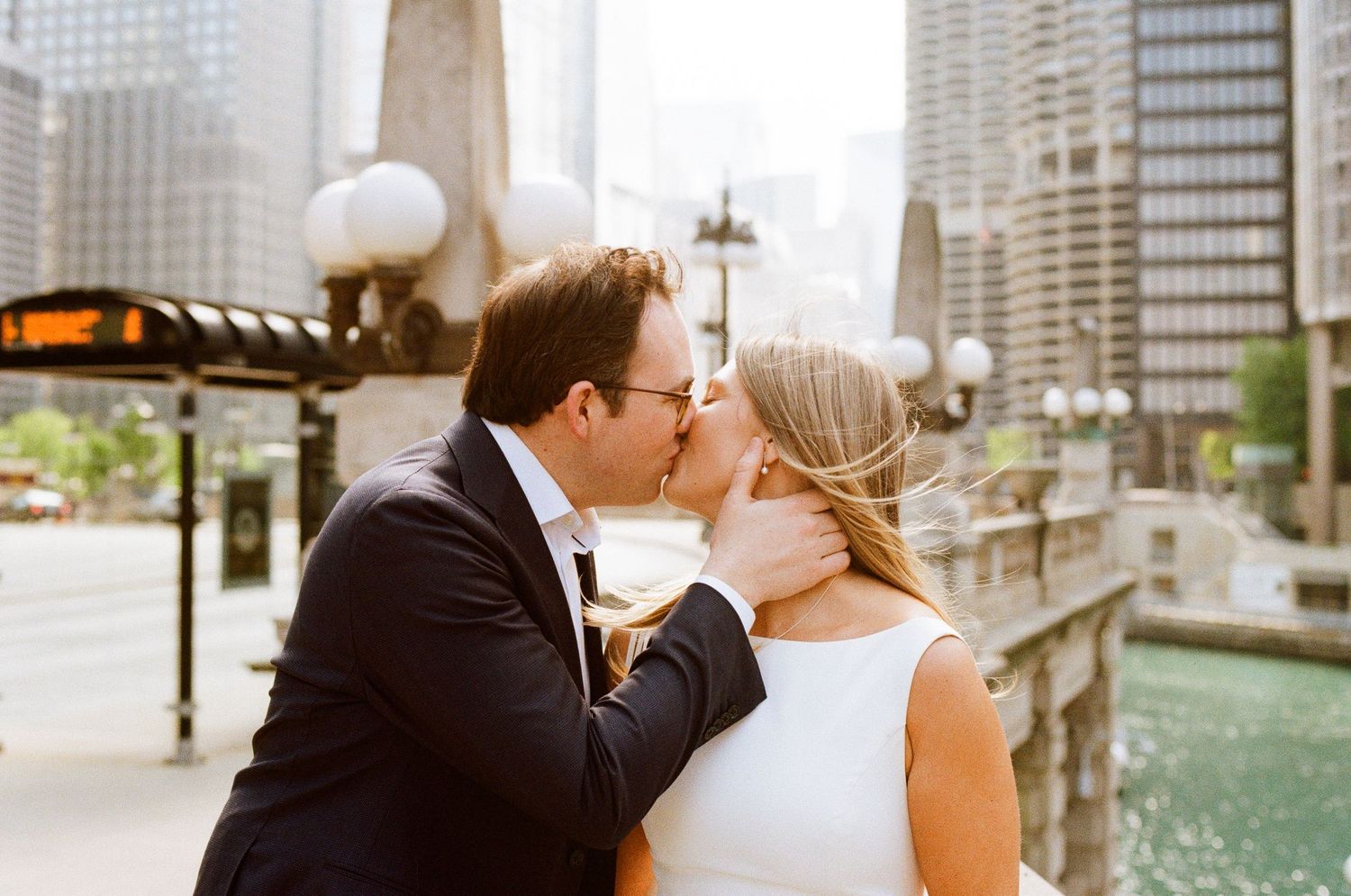 Couple sharing a romantic kiss on a Chicago Riverwalk bridge, surrounded by city skyscrapers on their wedding day.