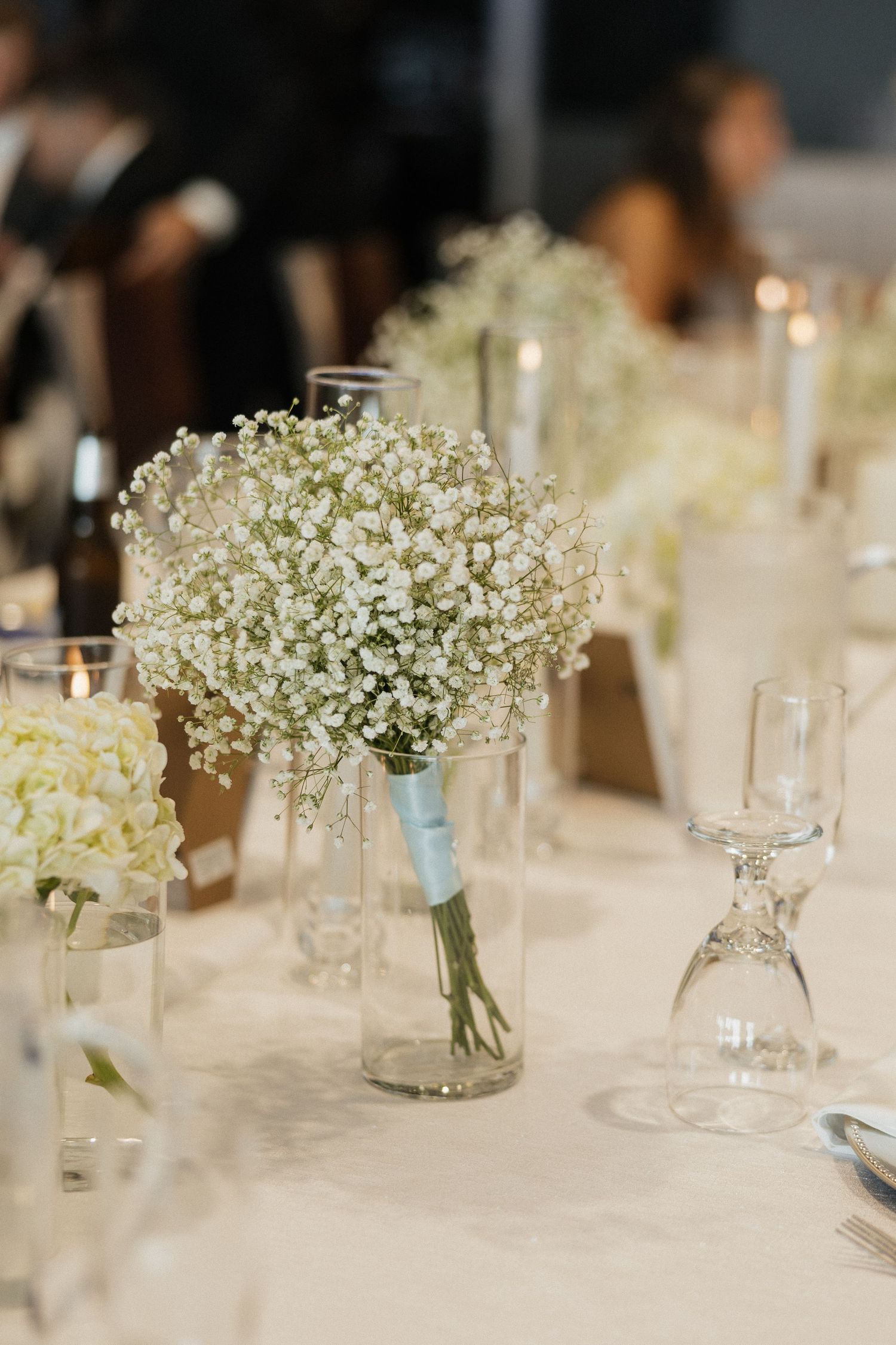 Elegant wedding table centerpiece featuring baby's breath bouquet in glass vase with blue ribbon accent.