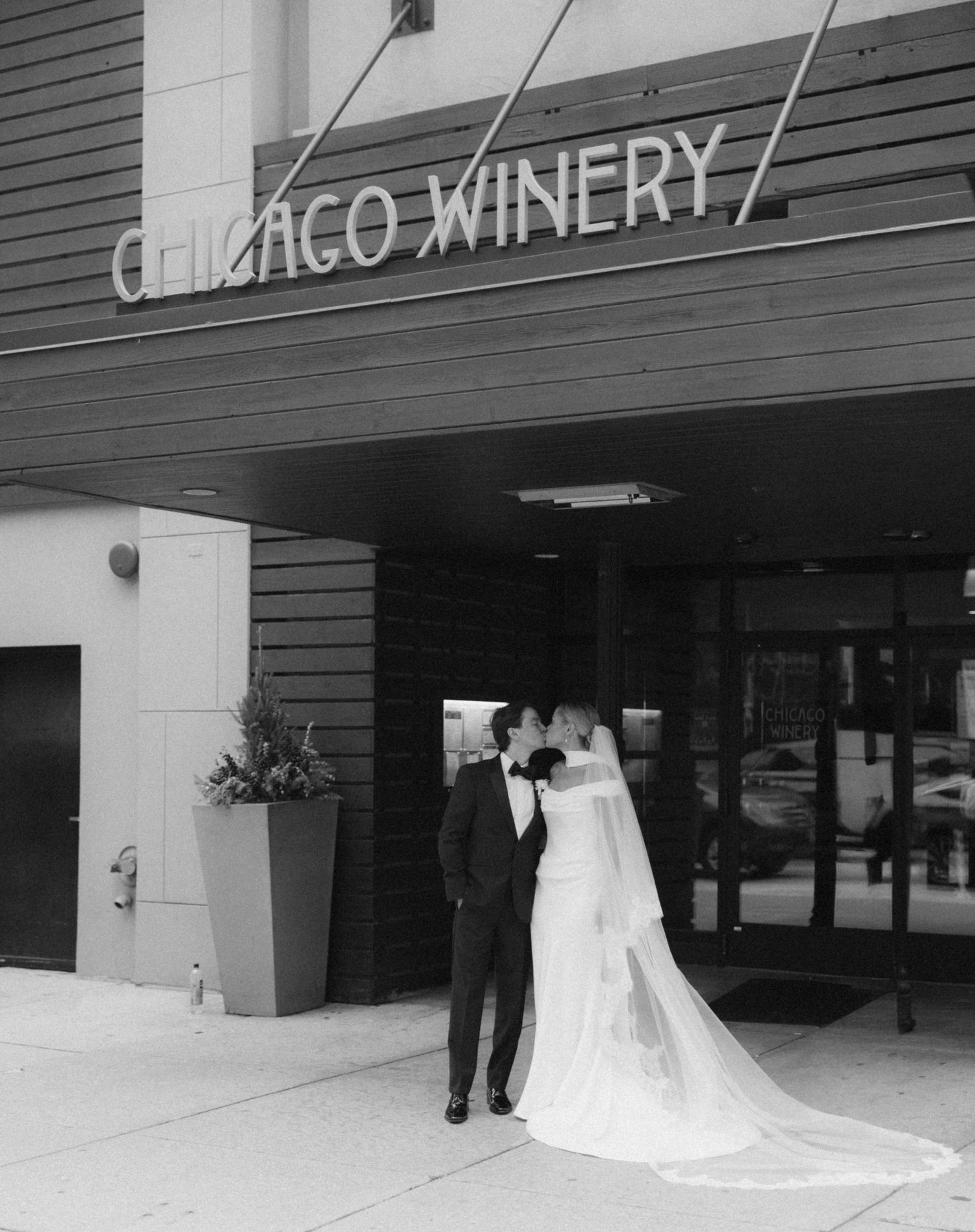 Bride and groom kissing outside Chicago Winery venue entrance in black and white wedding photo.