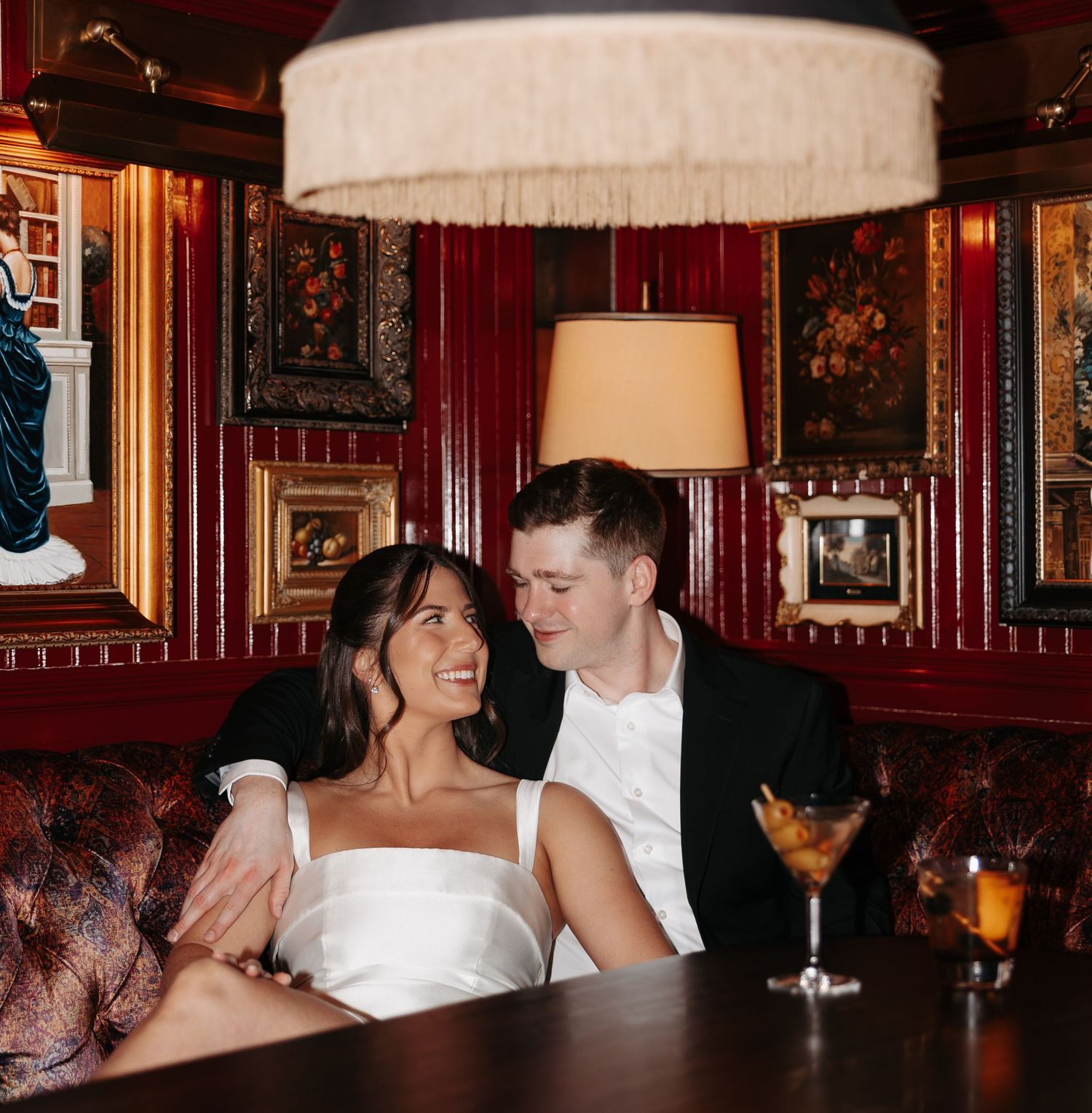 Couple in formal attire sharing intimate moments in an elegant restaurant with dark wood paneling and warm lighting.