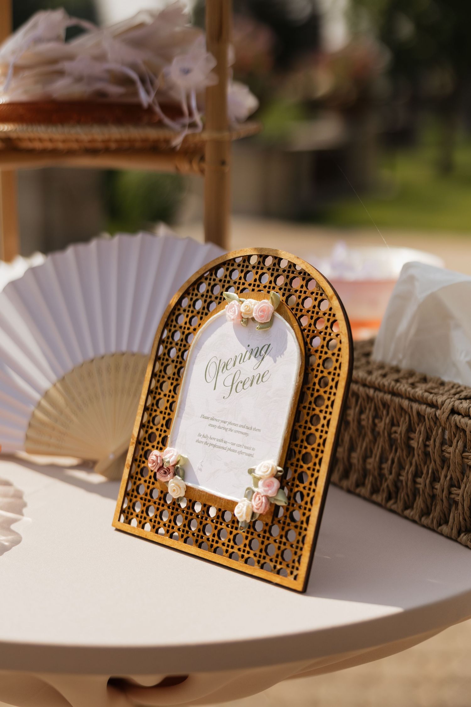Elegant arched laser-cut wooden wedding sign with floral accents reading Opening Scene, displayed on a white table outdoors.