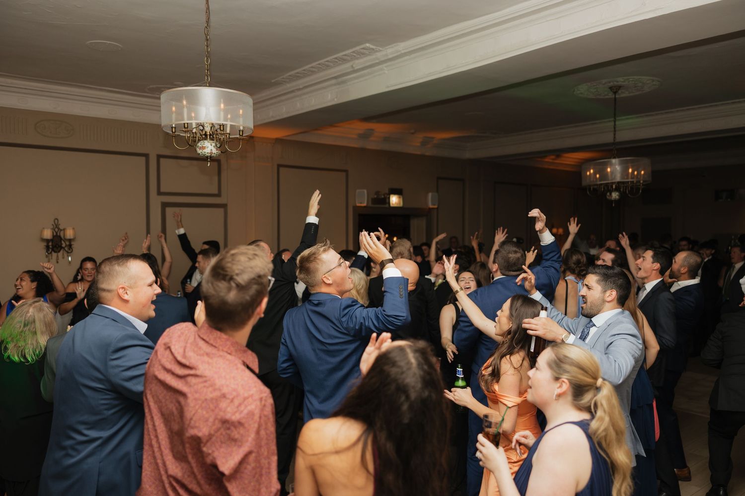 Guests dancing and celebrating with hands raised at a lively wedding reception in an elegant ballroom.