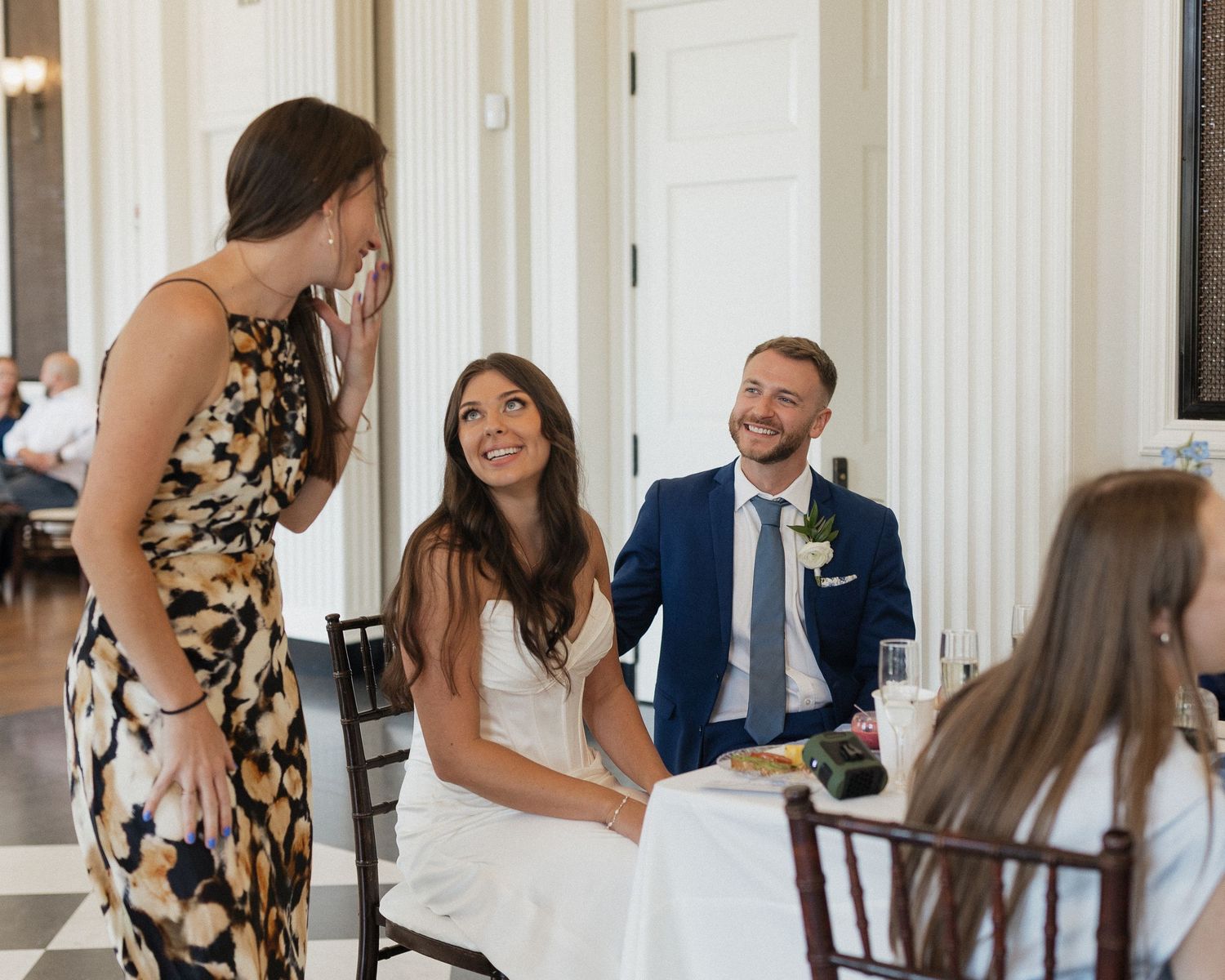 A couple shares a joyful moment in an elegant white columned hallway.