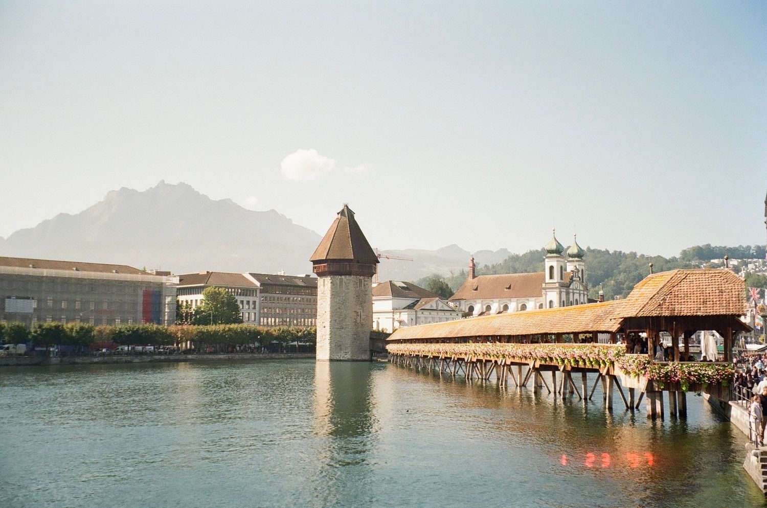 Historic wooden Chapel Bridge spans Lake Lucerne with mountains and city architecture in the background.