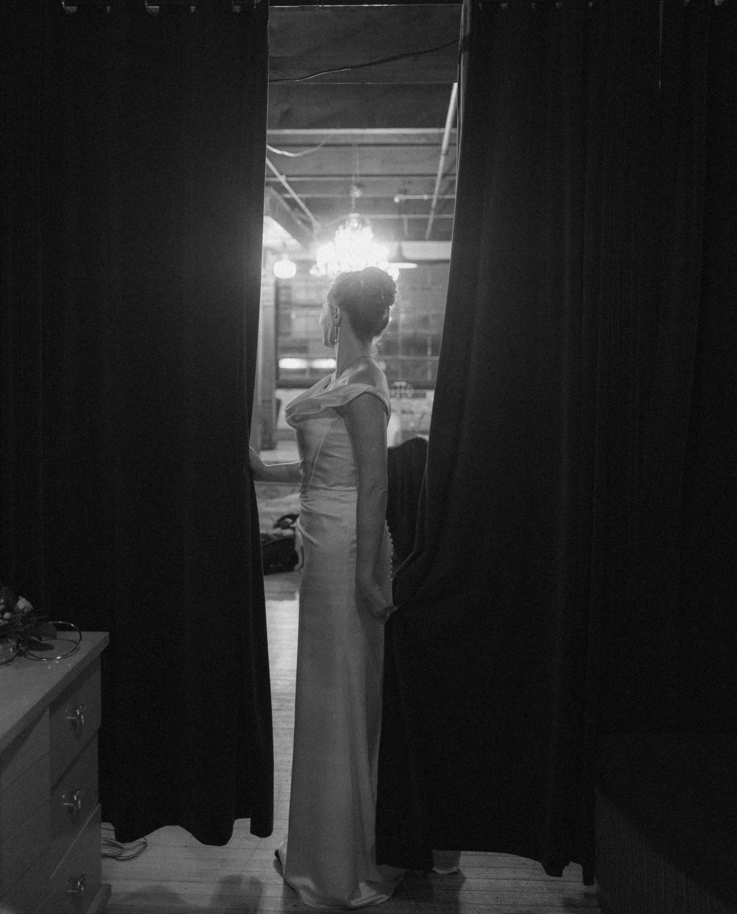 A series of black and white photos showing someone in a long dress standing against dark curtains in a dimly lit space.