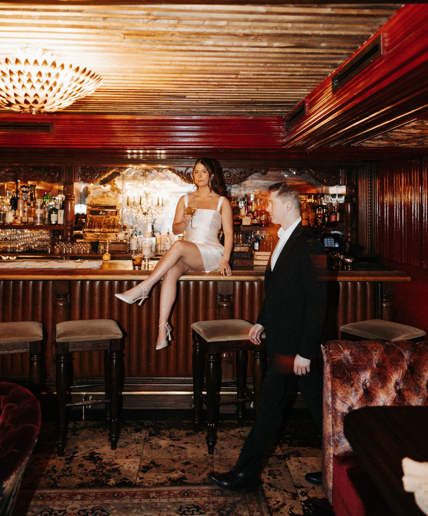 Elegant couple shares romantic moments in a dimly lit vintage bar with wood paneling and retro decor.