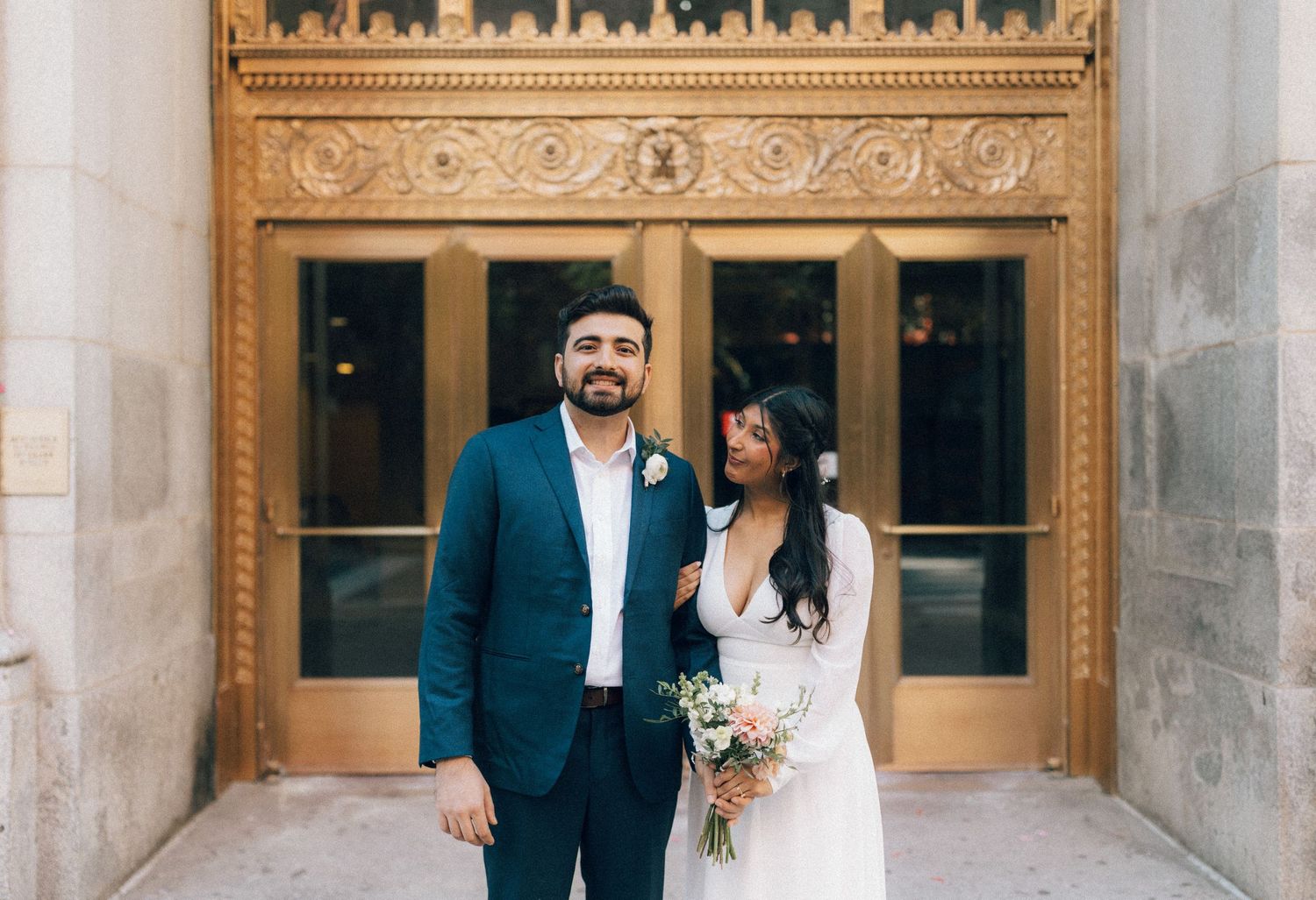 Bride and groom pose together in elegant formal attire at a historic venue with ornate architectural details.
