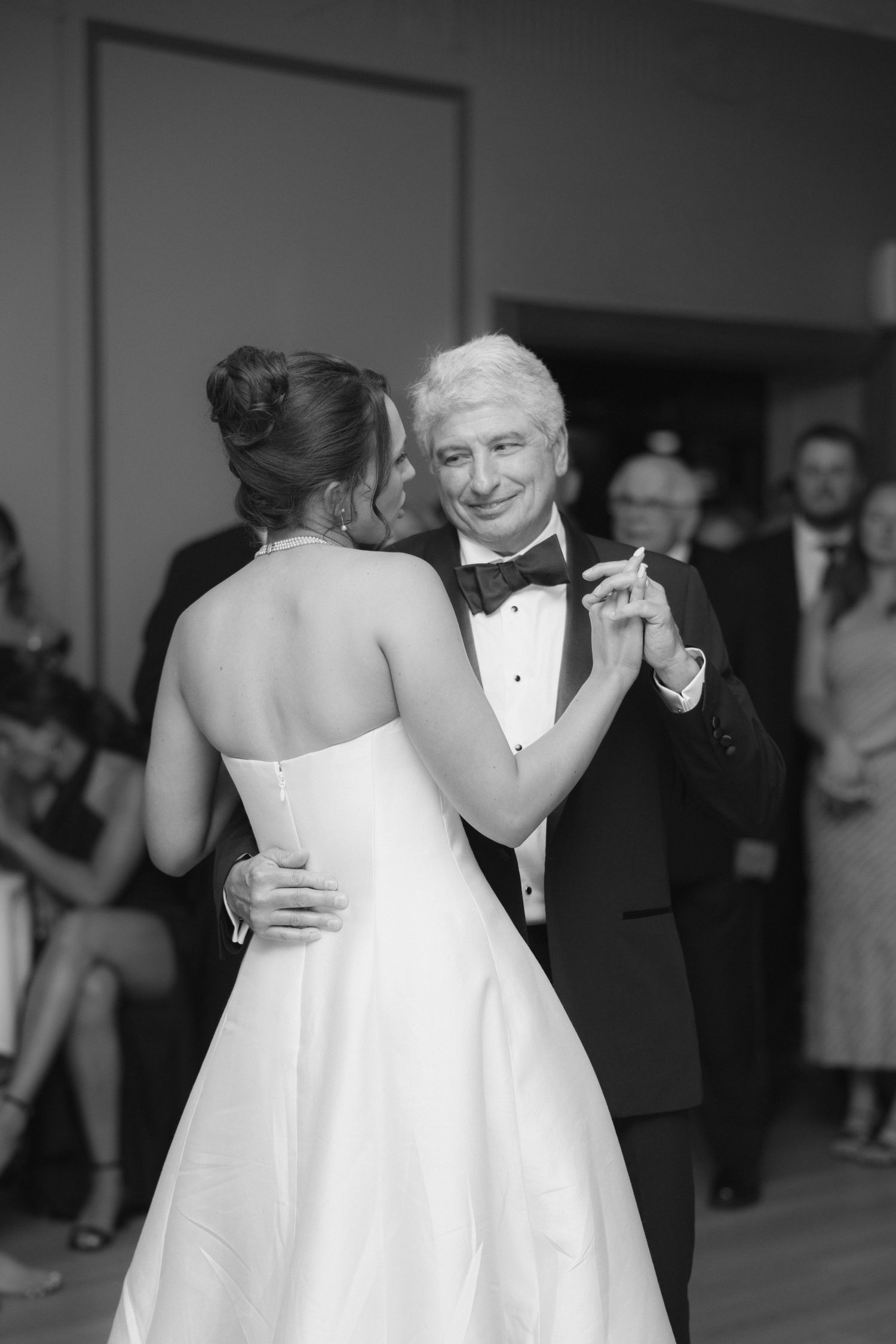 Black and white photo of a bride and older man sharing a father-daughter dance at a wedding reception.