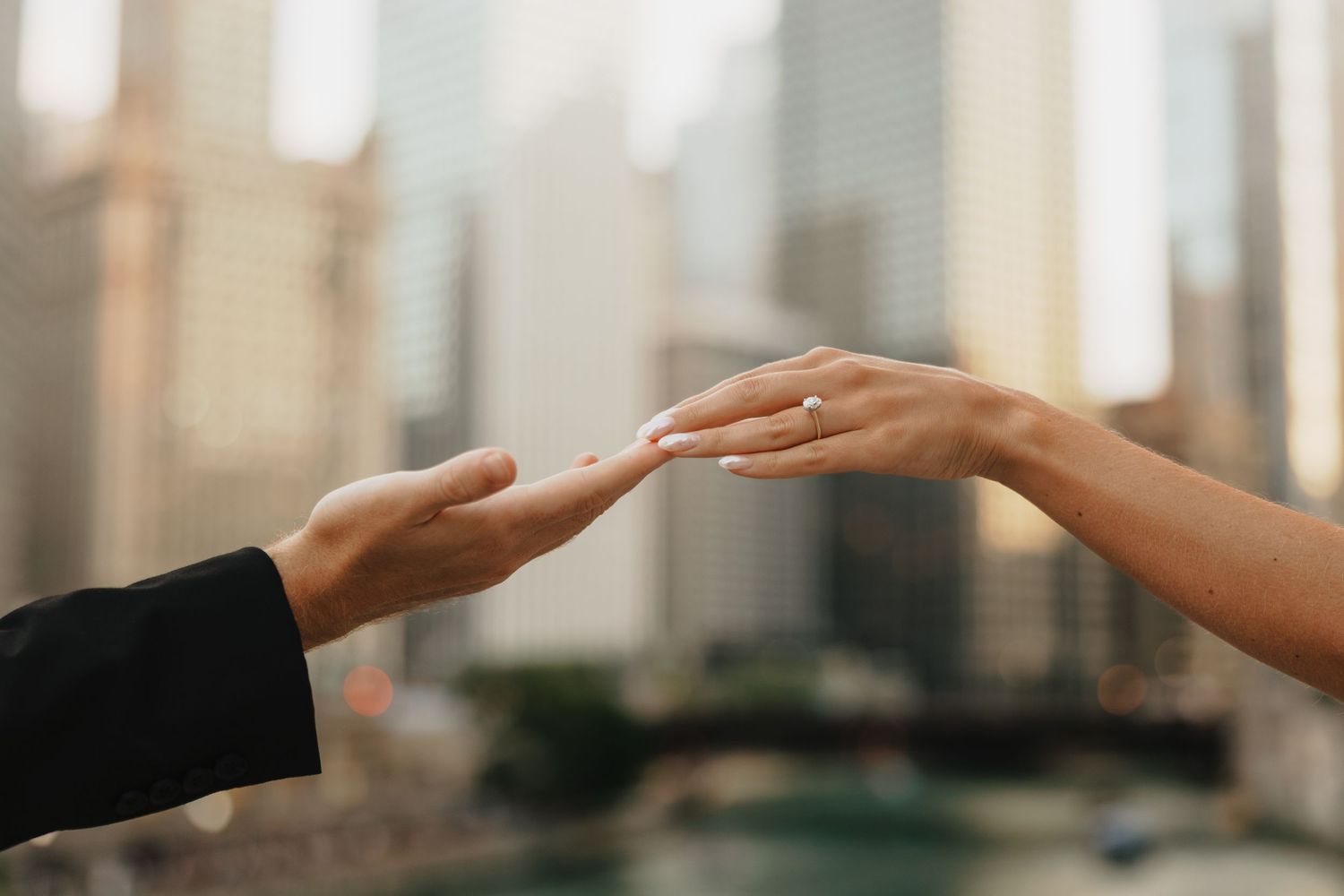Two hands reaching toward each other with engagement ring, city skyline backdrop, romantic urban moment.