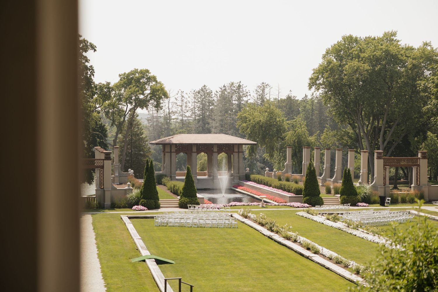 Elegant formal garden with fountain, gazebo, manicured lawns, and classical columns at an outdoor wedding venue.