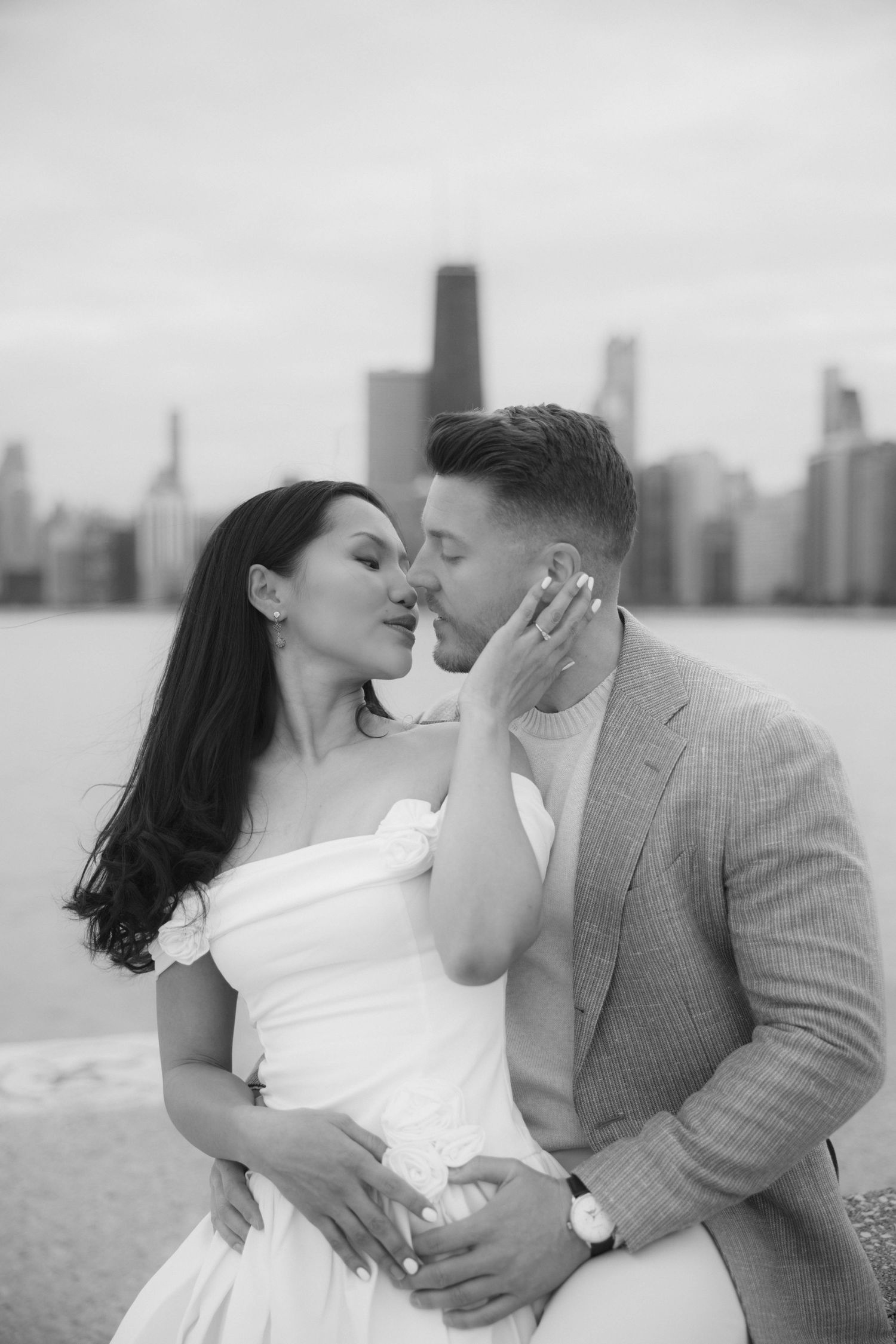 Black and white photo of couple sharing romantic kiss with Chicago skyline visible behind them.