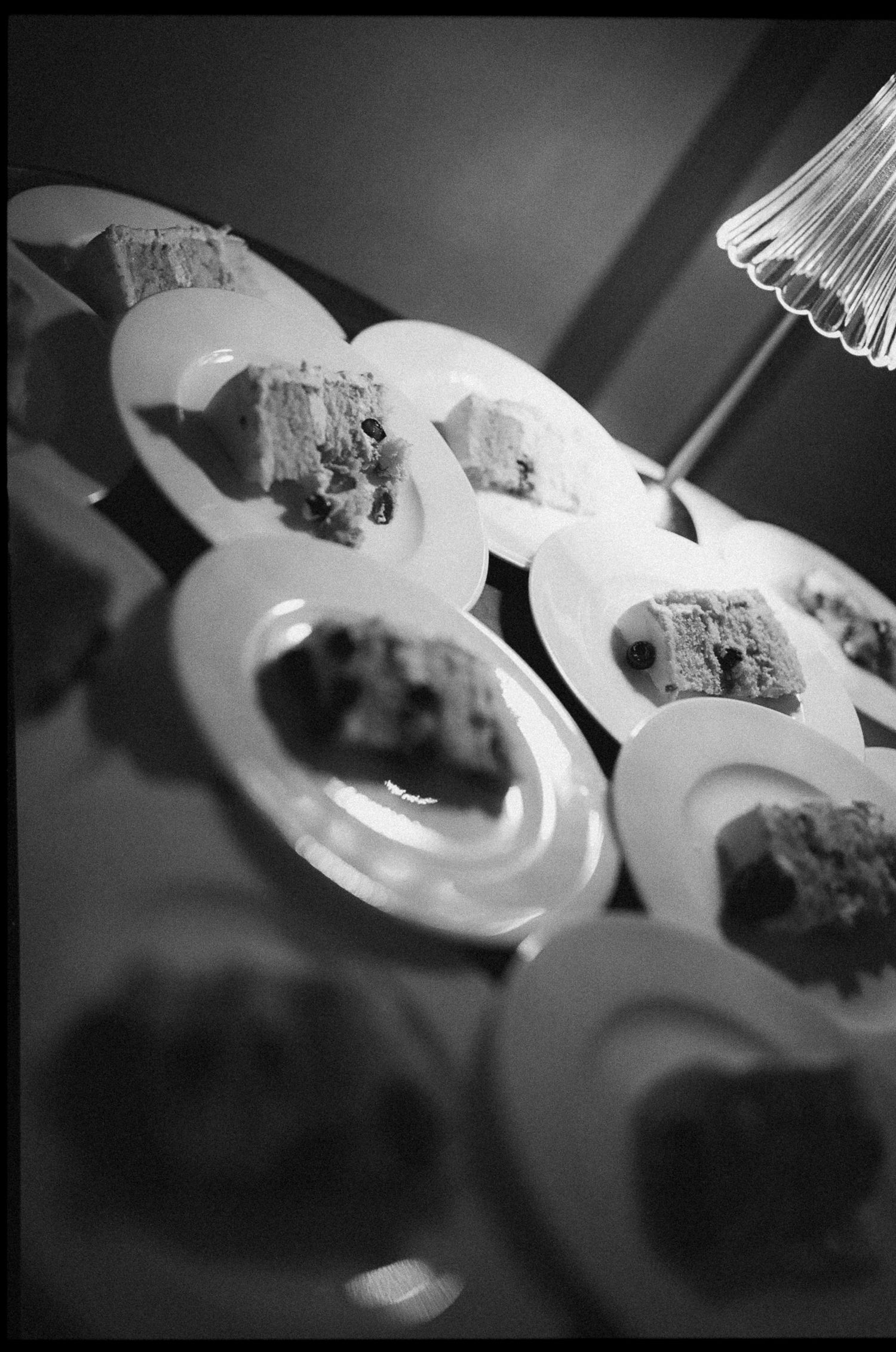 Black and white photo of multiple white plates with sliced cake pieces arranged on a table at a reception.