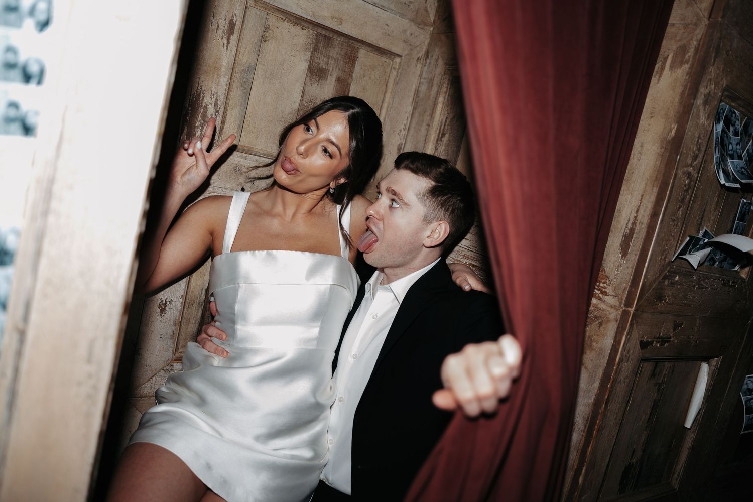 Two people dance and laugh together at a party, with one wearing a white dress and the other in a black suit.