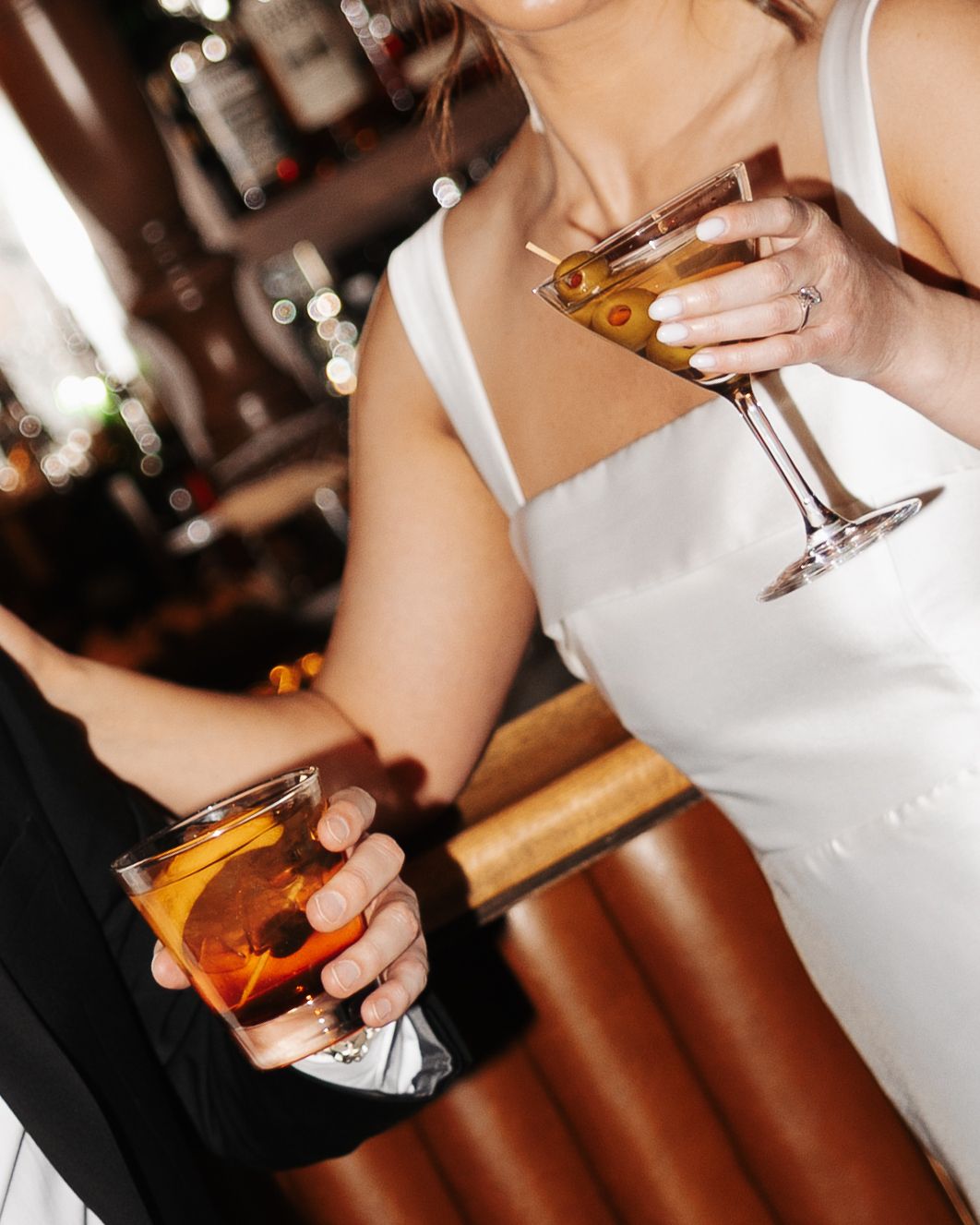 Person in white dress holding a cocktail glass at a dimly lit bar or event venue.
