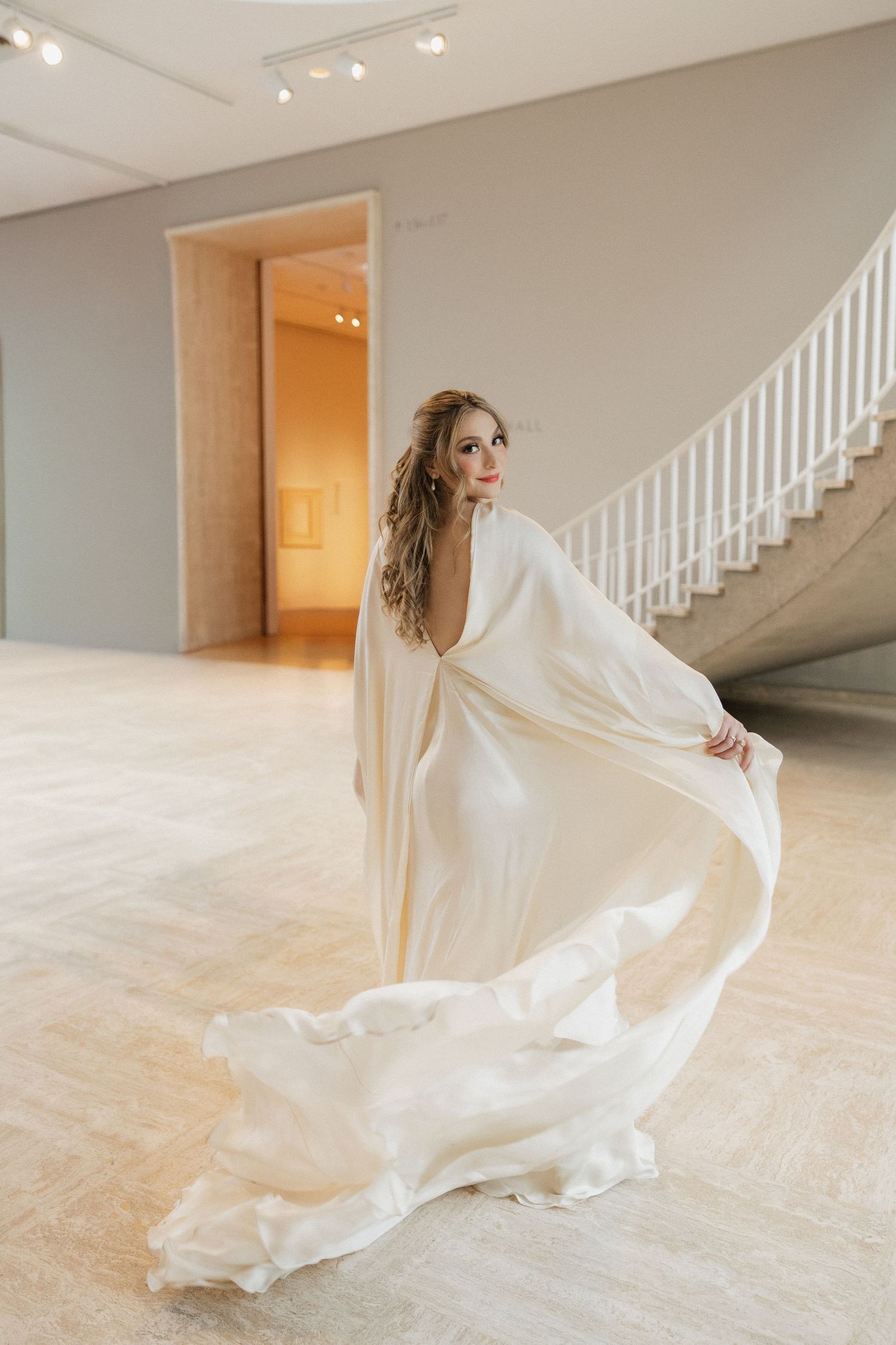 A flowing white wedding dress twirls gracefully in a light-filled room with white stairs and hardwood floors.