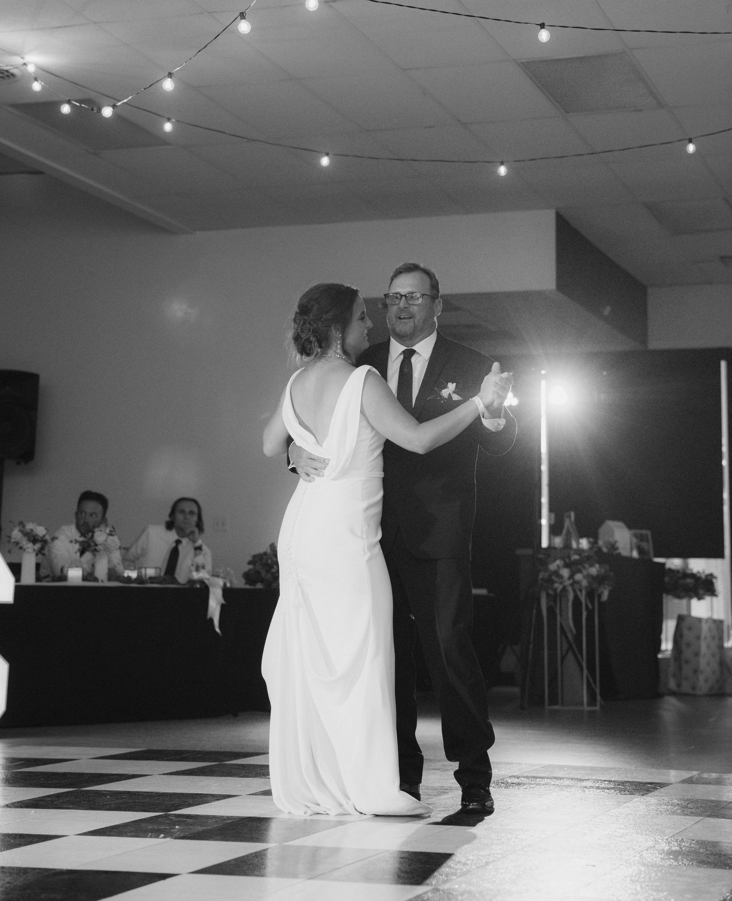 Couple dancing their first dance at a wedding reception under twinkling string lights.