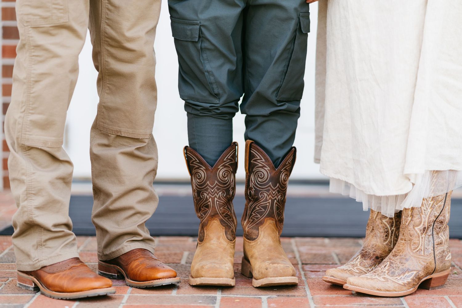 Close-up of three people wearing cowboy boots and casual attire standing on brick pavement.