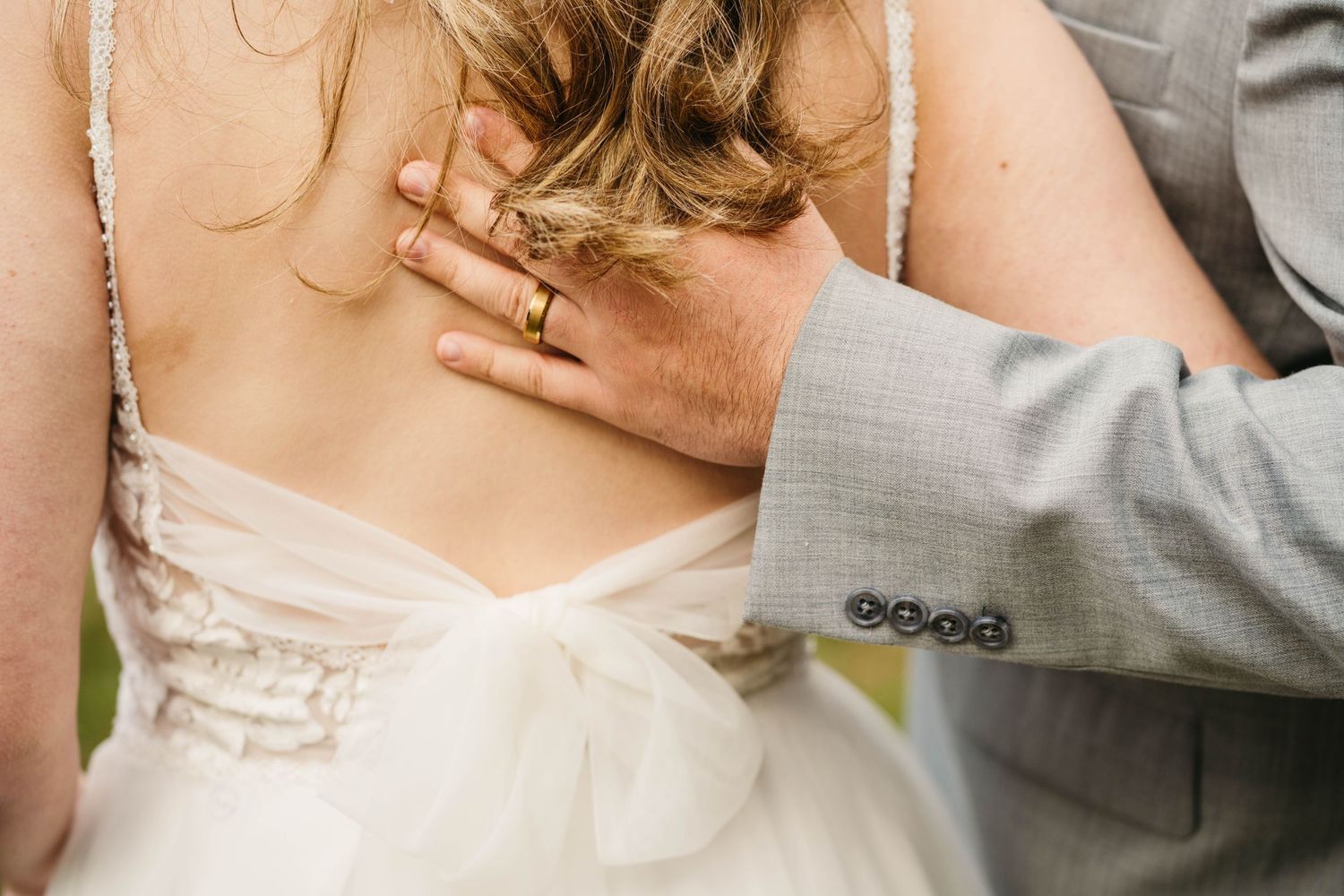 Groom in gray suit placing hand on brides lace back dress during wedding celebration.