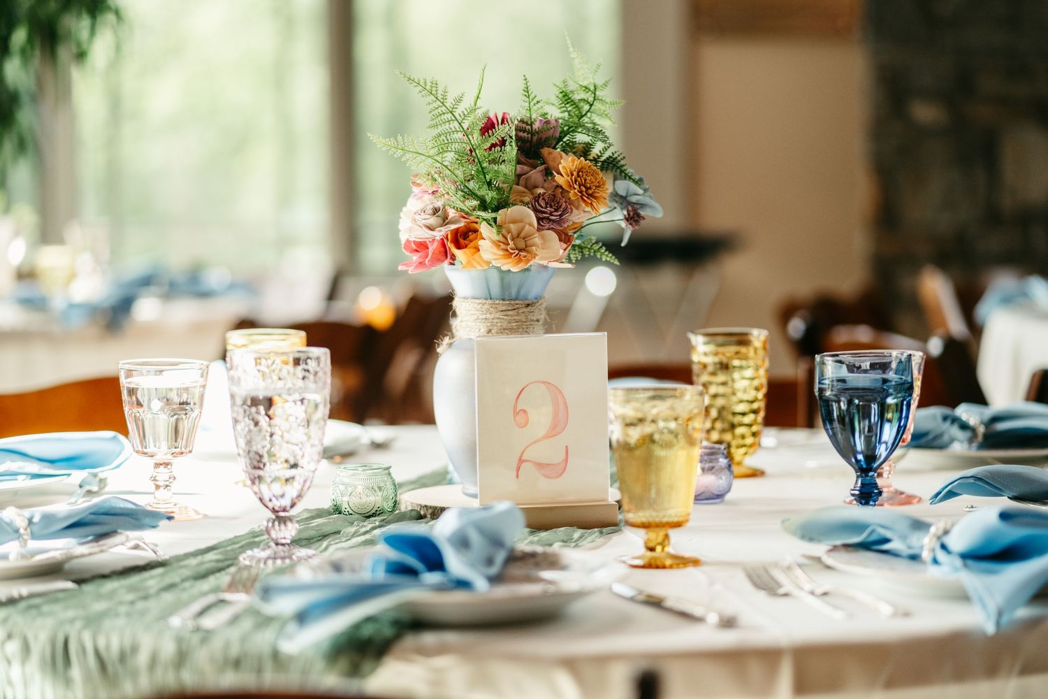 Elegant wedding table setting with floral centerpiece, colorful glassware, and blue napkins.