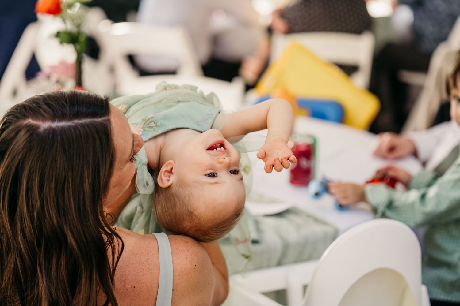 Mother tenderly holding and kissing her laughing baby at a wedding reception.