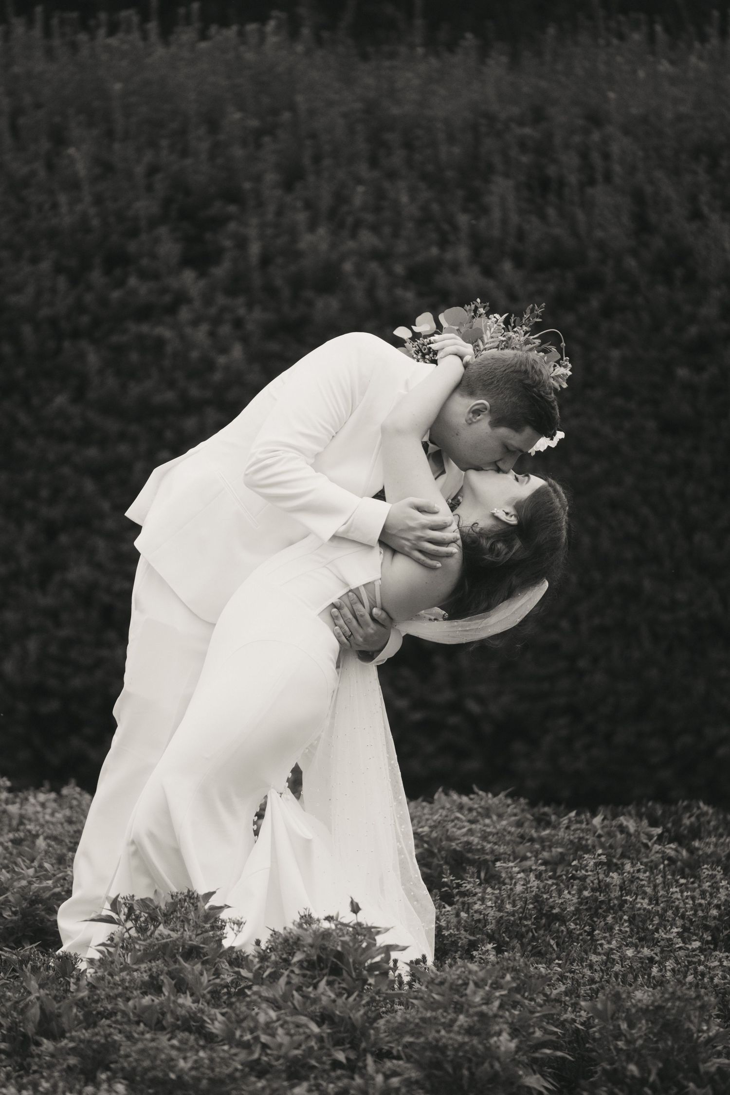 Black and white photo of groom dipping bride for a romantic kiss outdoors at wedding.