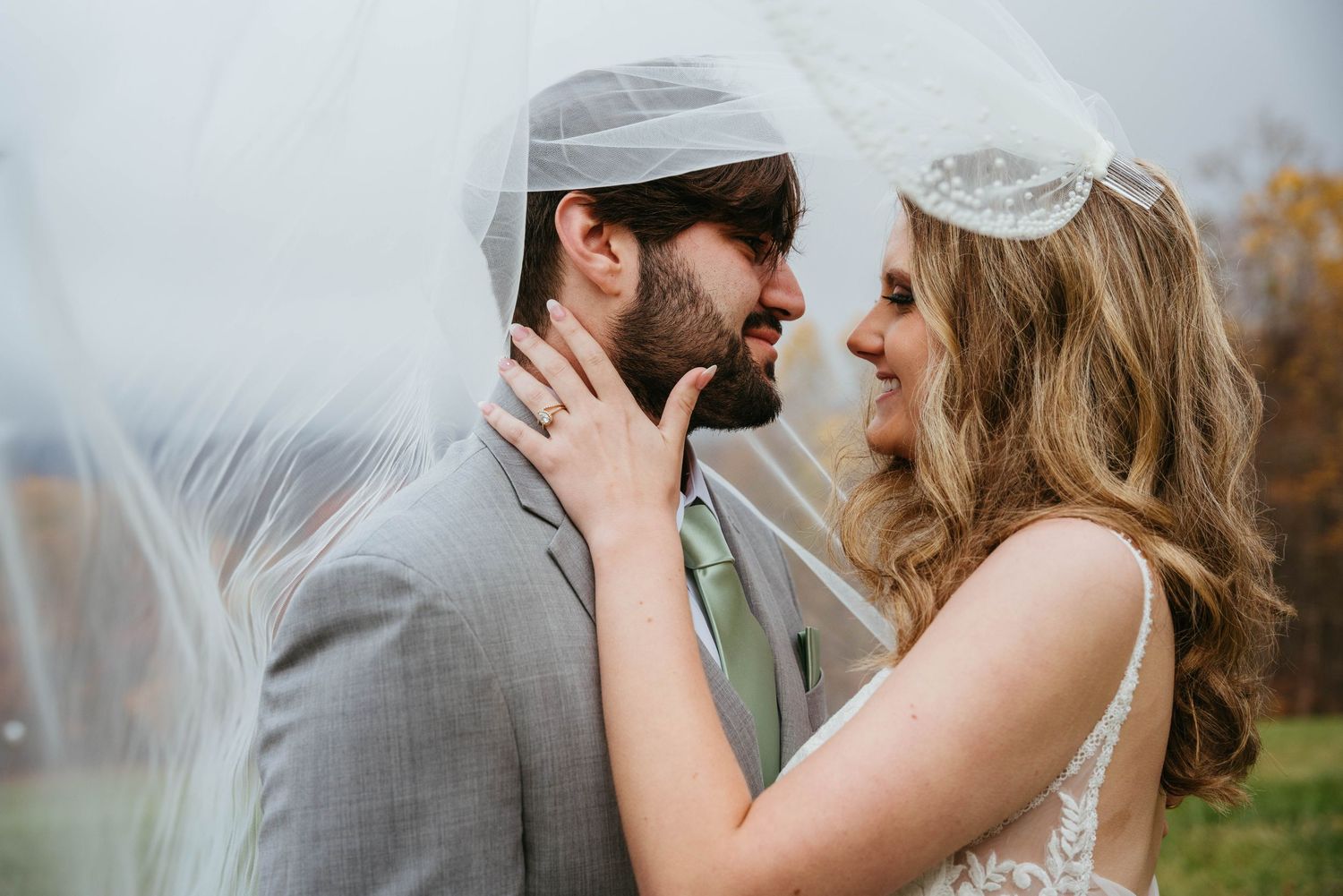 Bride and groom share a romantic moment under a flowing veil, smiling at each other on their wedding day.