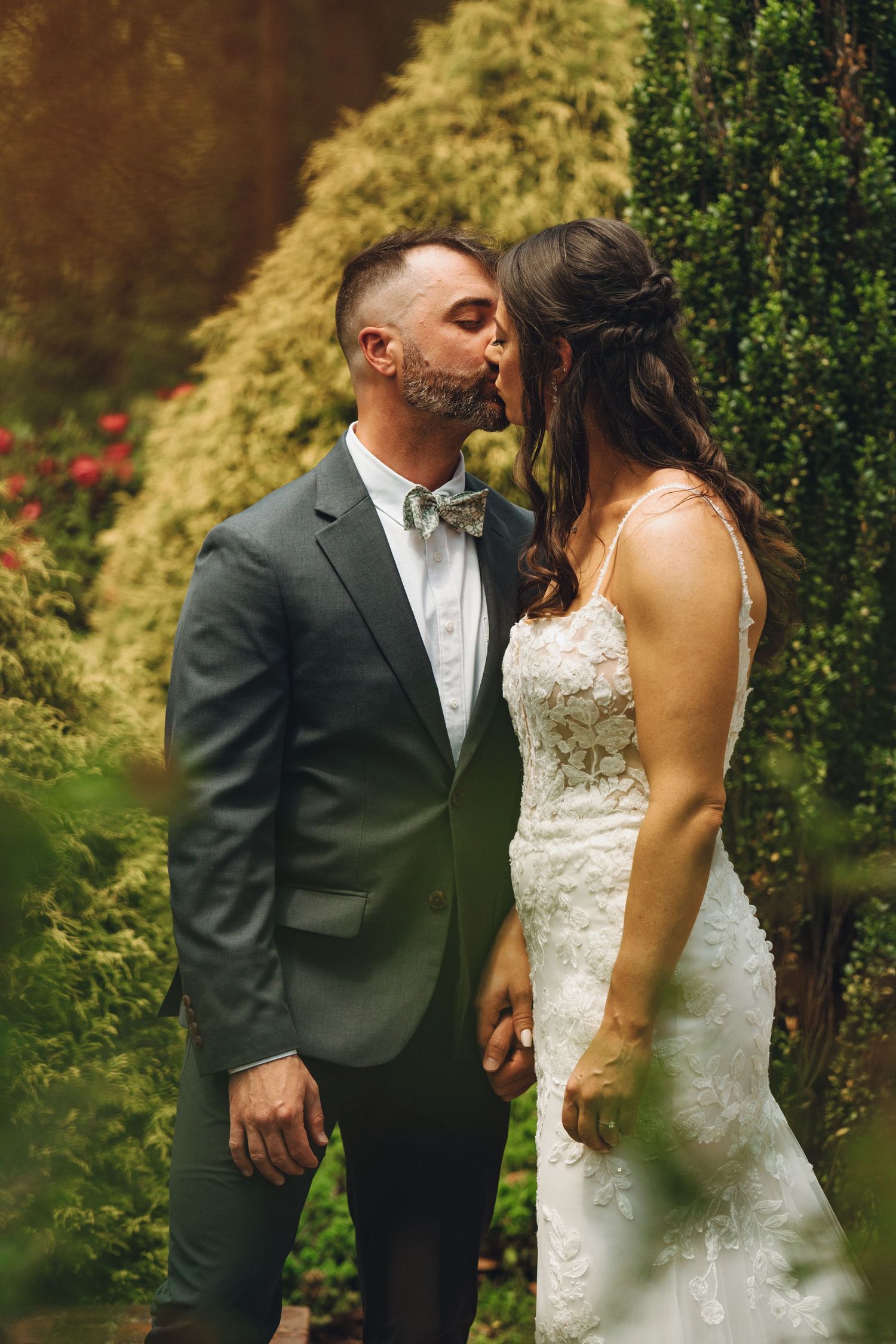 Bride and groom sharing a romantic kiss in a lush green garden.