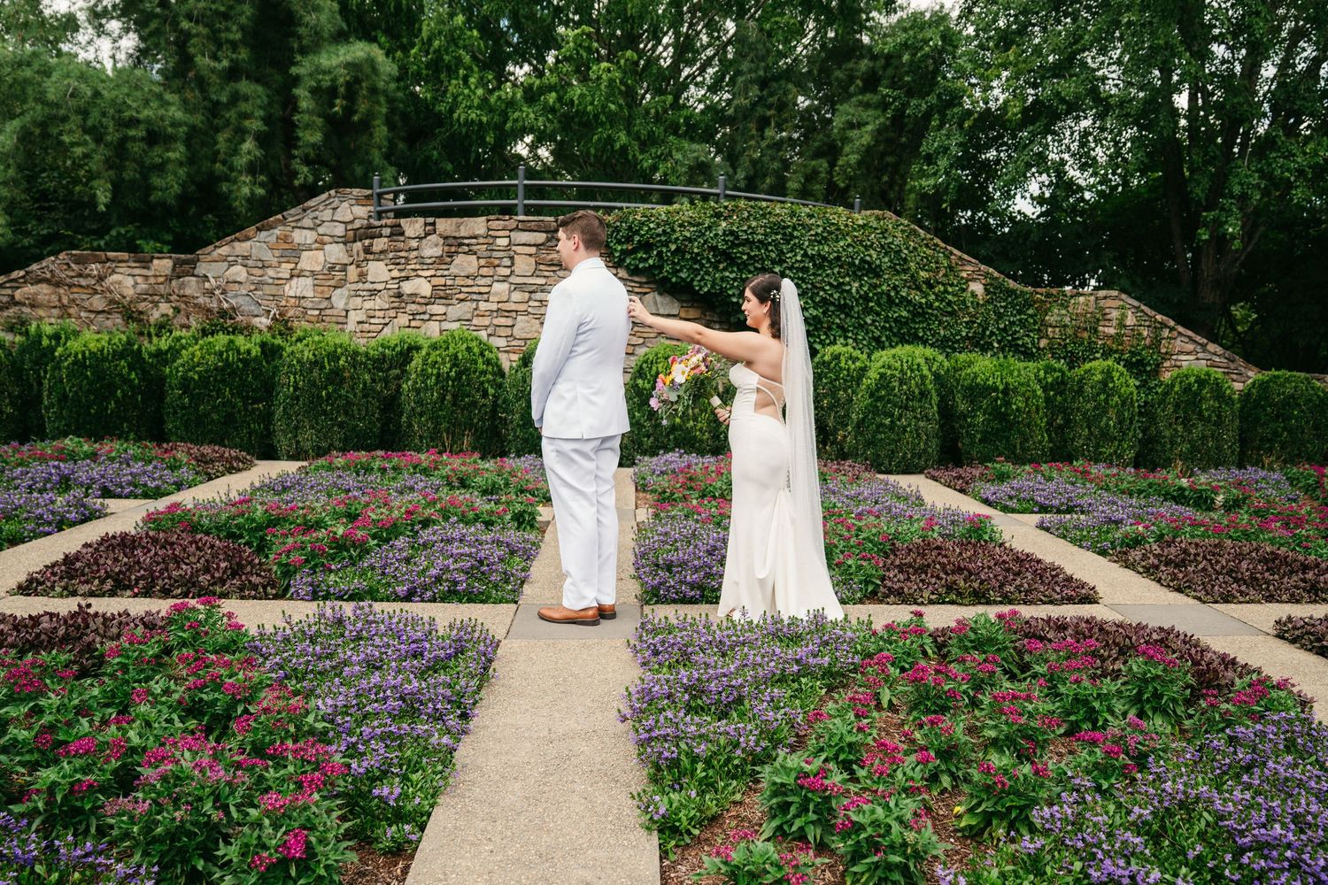 Bride and groom dancing together in a colorful formal garden with lush hedges and flowers.
