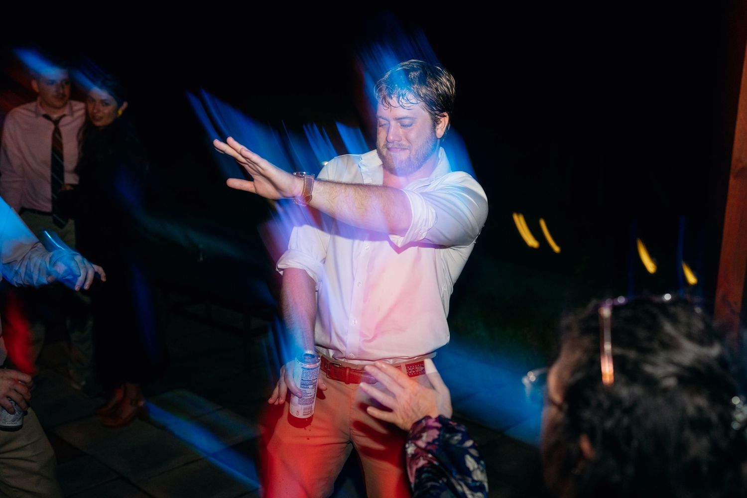 Man in white shirt and orange pants dancing energetically under blue party lights.