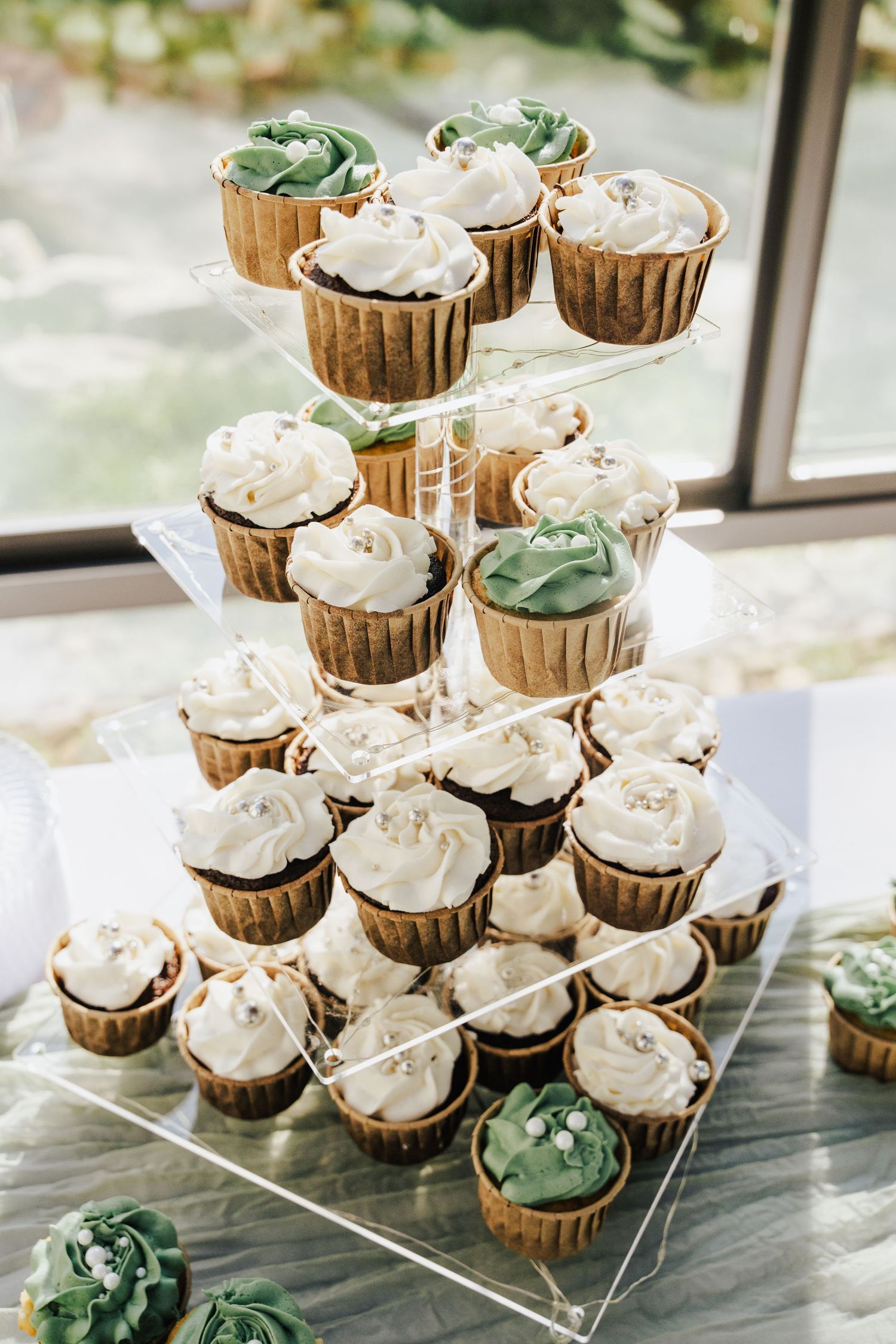 Elegant tiered acrylic stand displaying white and green frosted wedding cupcakes.