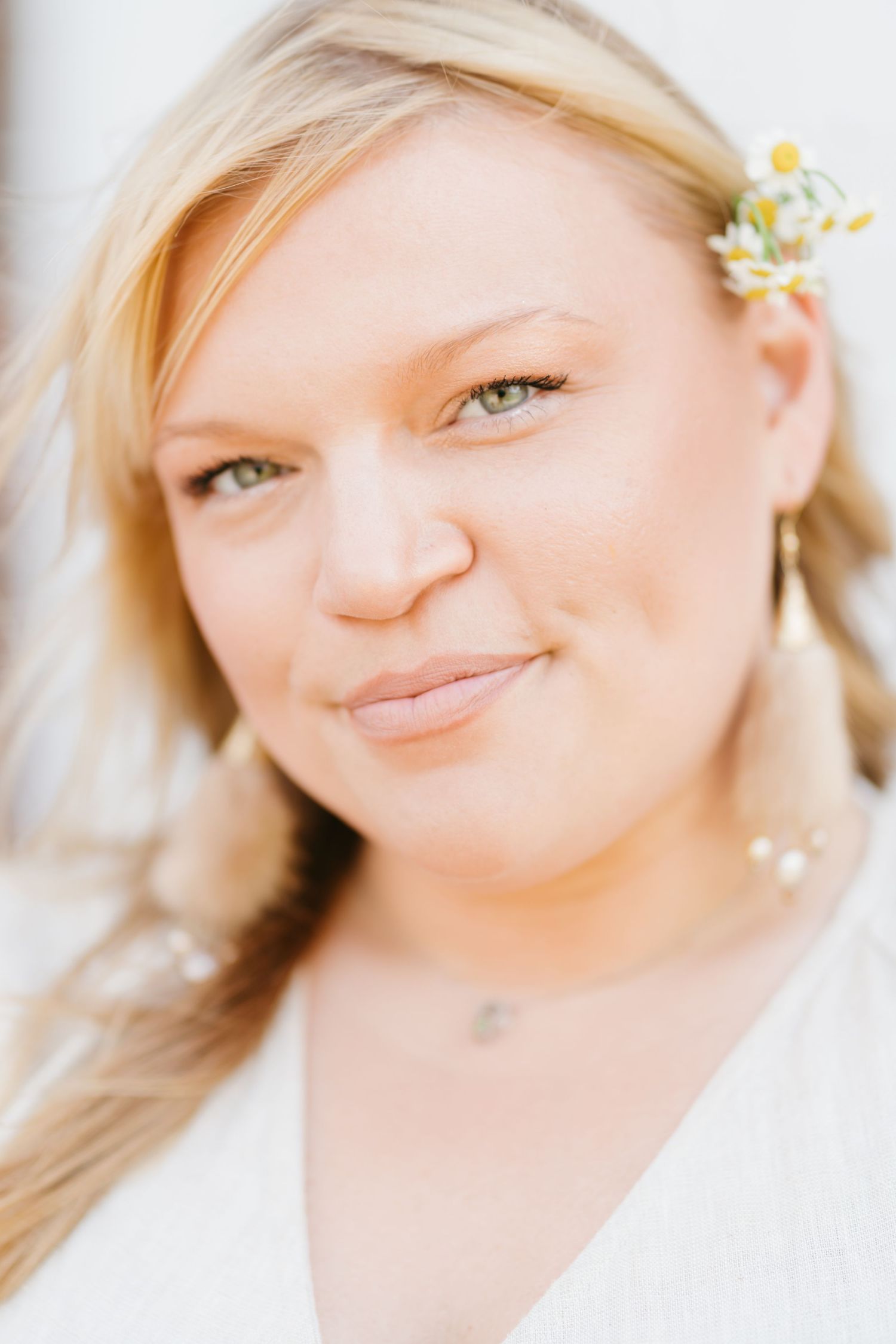 Close-up portrait of blonde bride with green eyes wearing small yellow flower hair accessory.