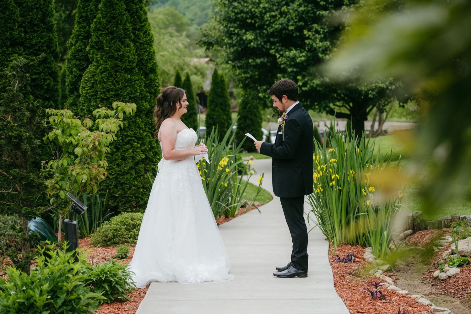 Bride and groom share intimate first look moment on garden pathway exchanging vows.