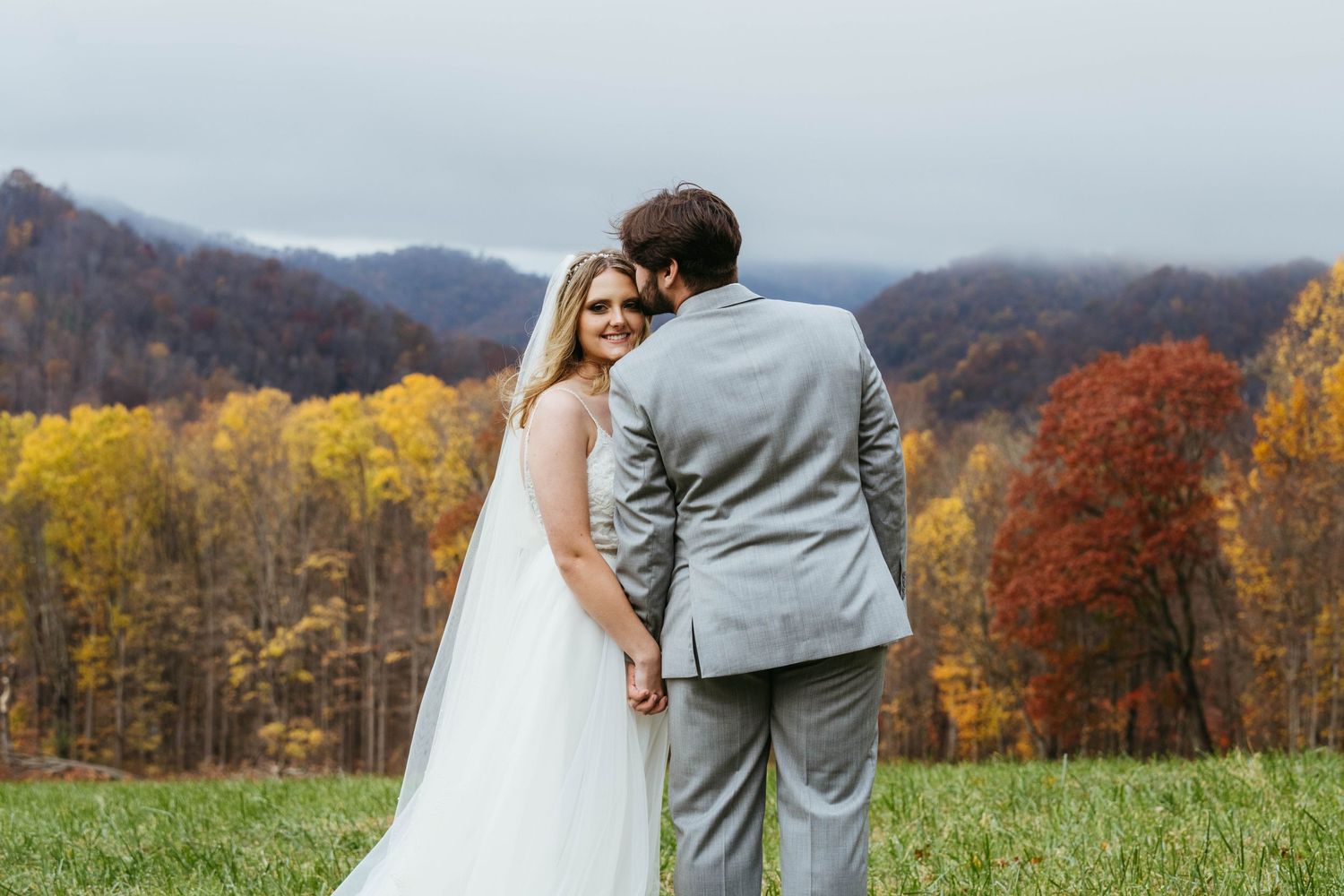 Bride and groom holding hands overlooking stunning autumn mountain landscape in colorful fall foliage.