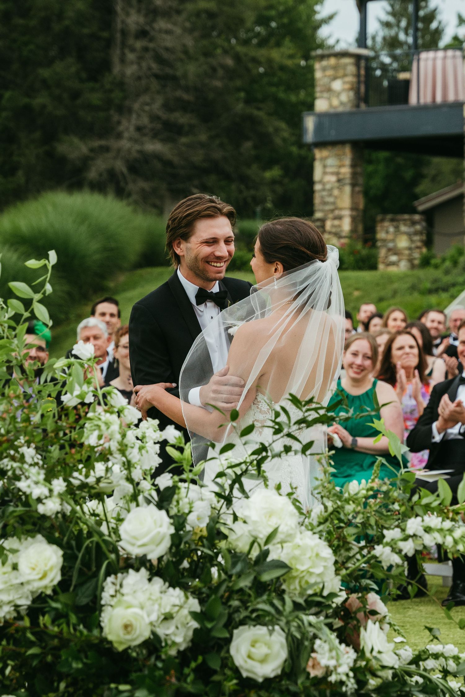 A joyful bride and groom share a romantic moment at the altar surrounded by lush white floral arrangements.