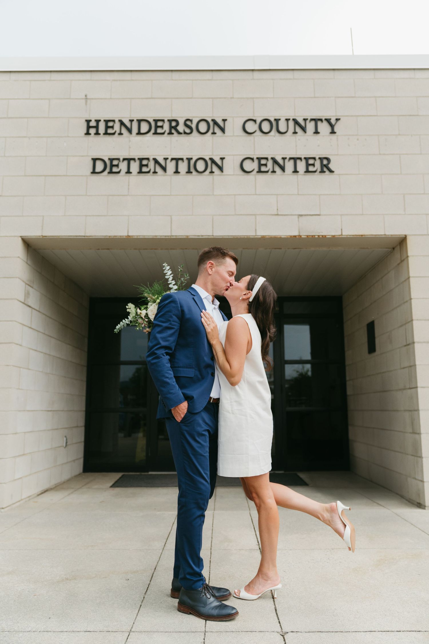 Newlyweds share a kiss outside Henderson County Detention Center in wedding attire.