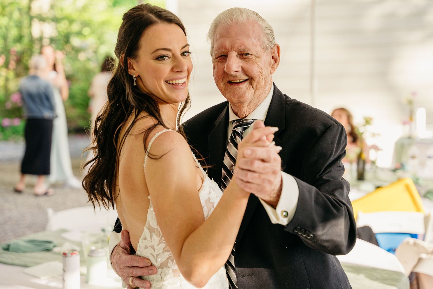 Smiling bride dancing with elderly grandfather in suit at wedding reception.