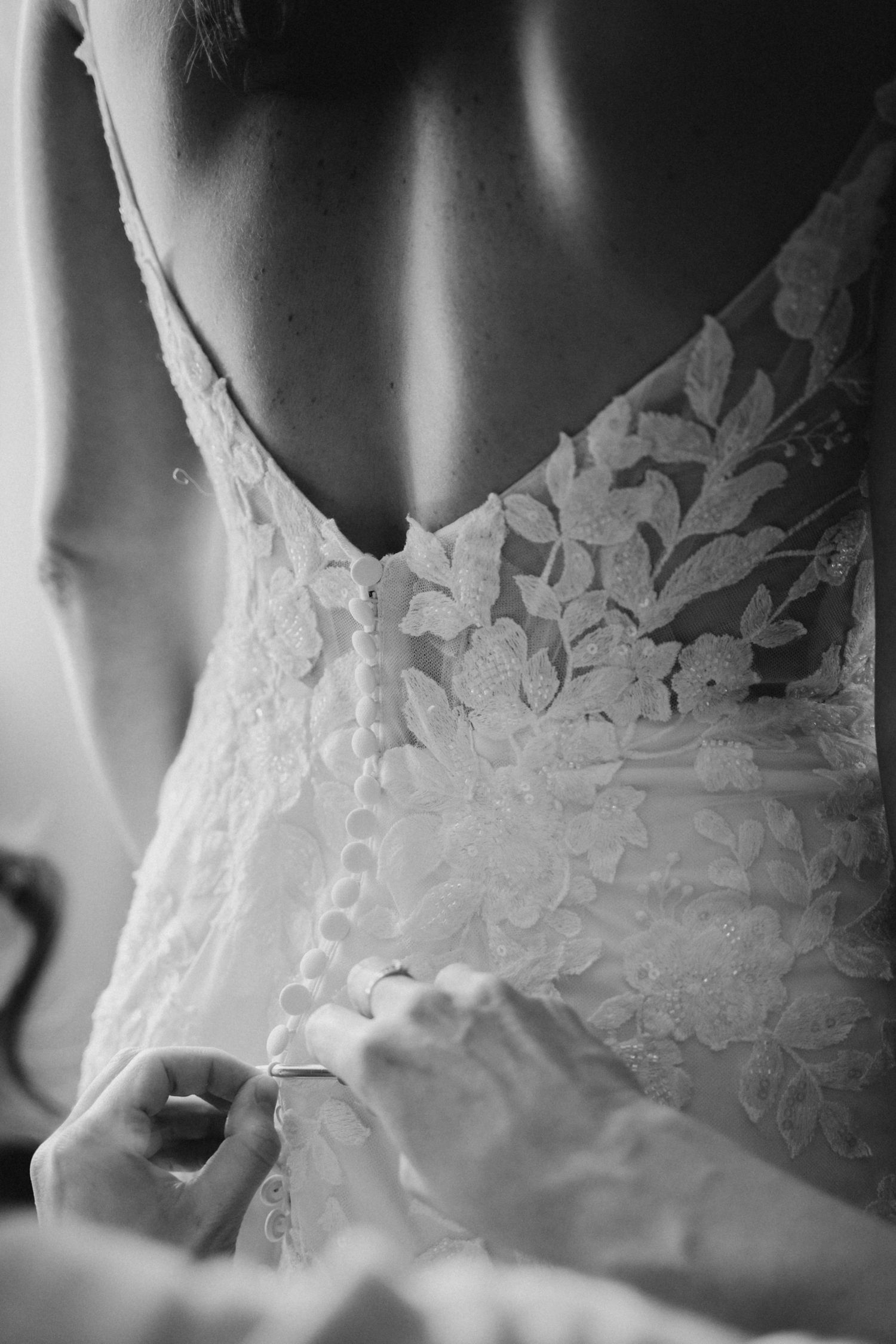 Black and white photo of bride having lace wedding dress buttoned up the back.