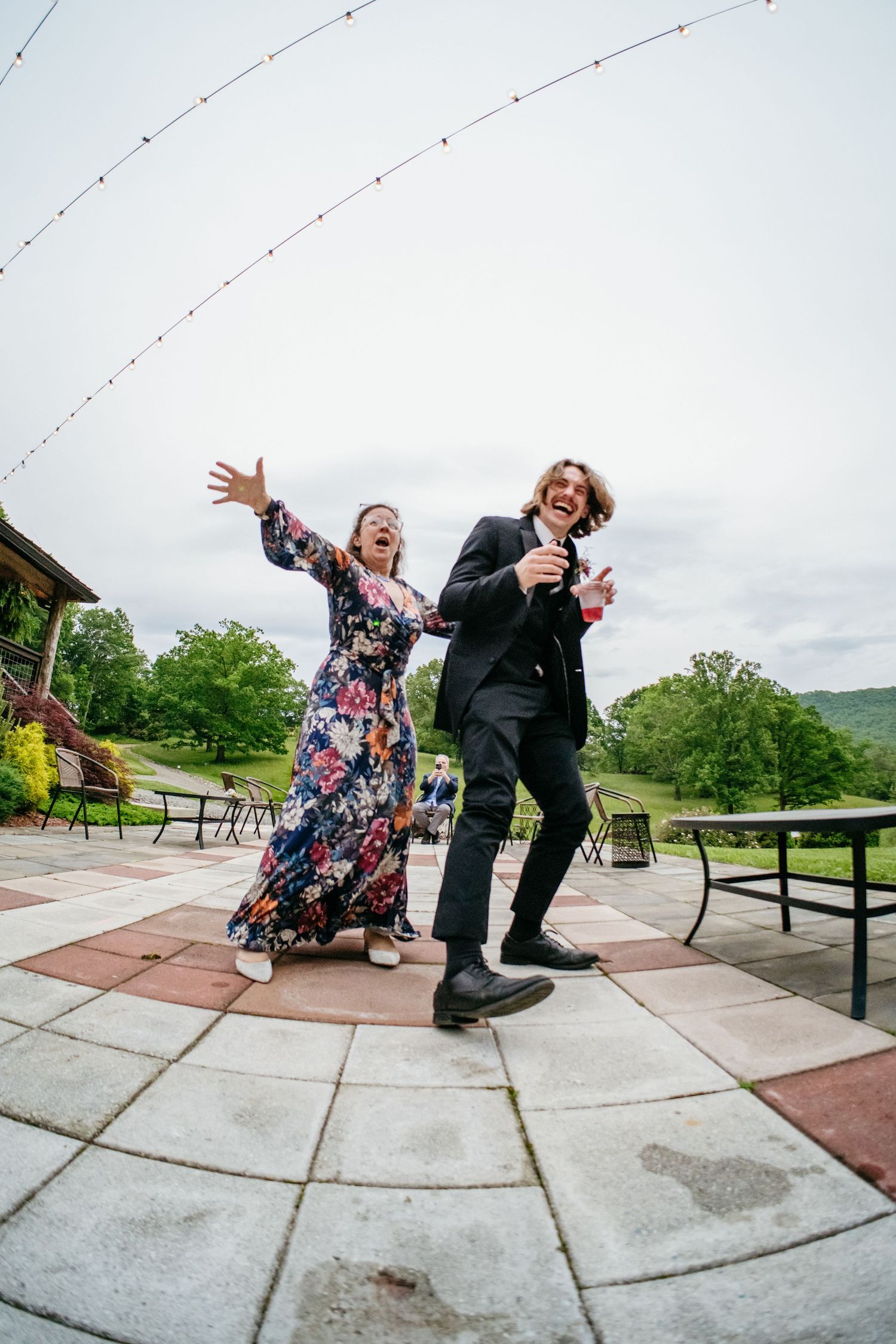 Excited wedding guests dance energetically on an outdoor stone patio with string lights overhead.