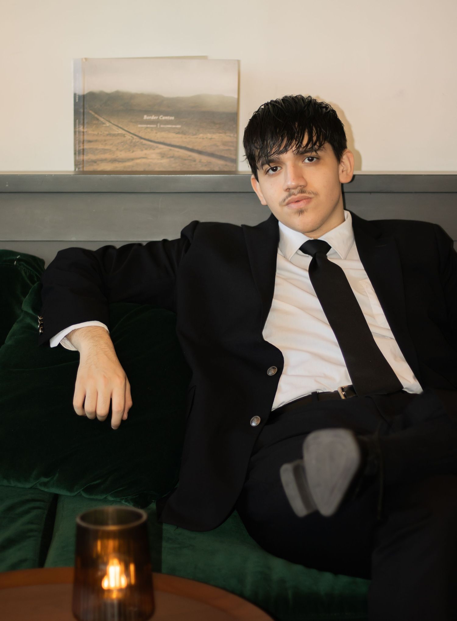 Portrait on green velvet couch with artwork and candle in elegant setting.