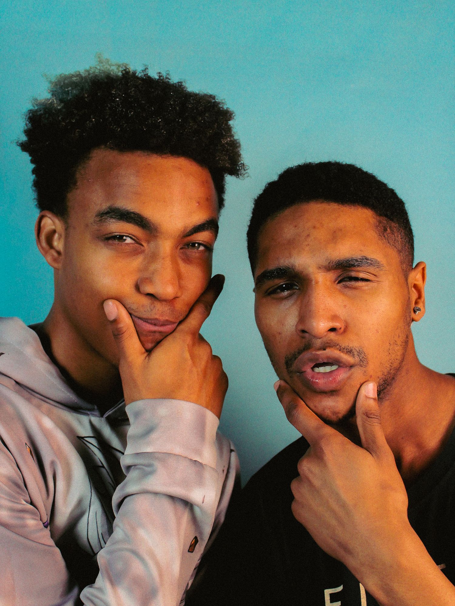 Two friends posing playfully with thoughtful expressions against a turquoise background.